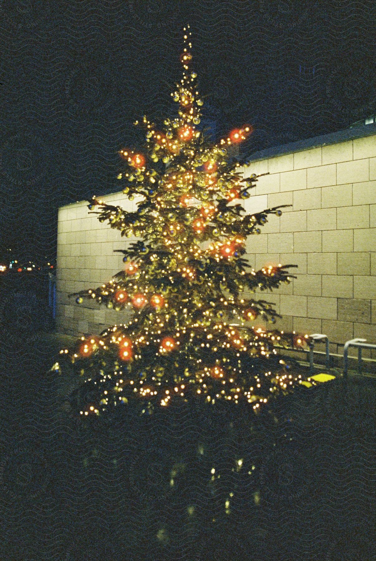 A brightly lit christmas tree stands on a quiet street at night