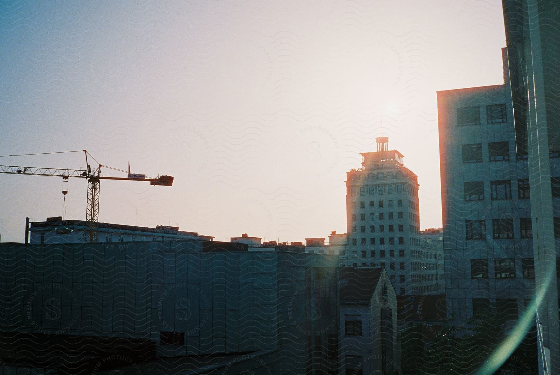 Sun rising over neboticnik skyscraper casting shadows on nearby tall apartment buildings and creating a silhouette of a crane on a roof