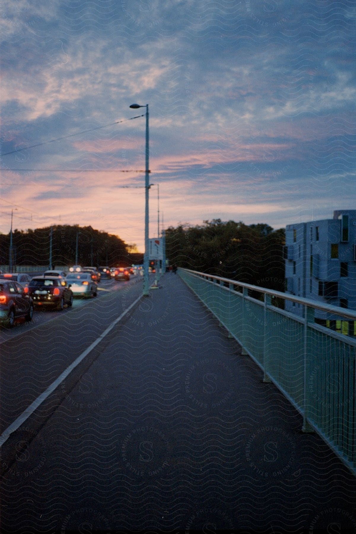 Traffic lined up on a highway at dusk near a city building separated by a steel railing