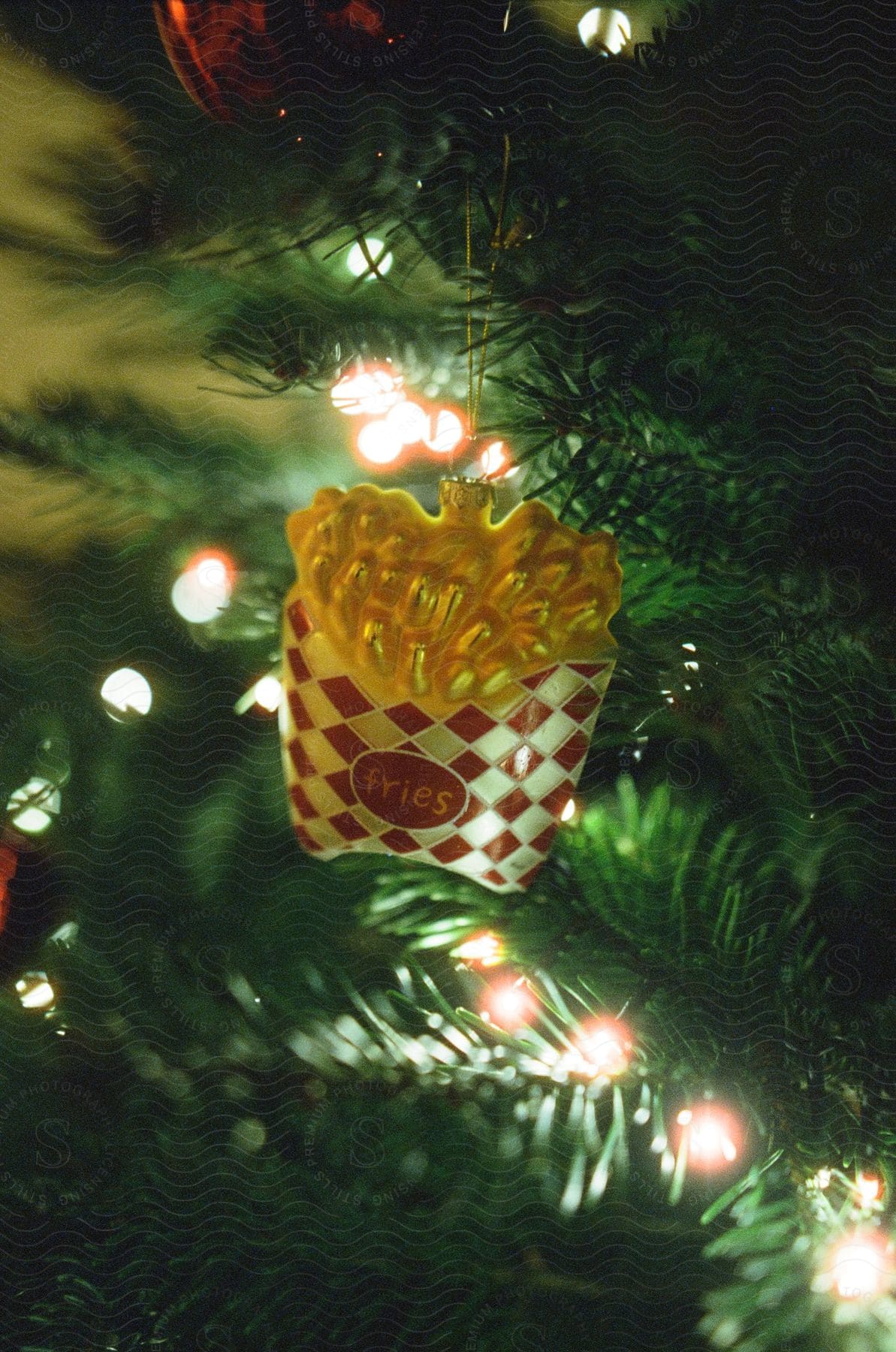 A christmas tree ornament resembling a fast food package of french fries hanging on a tree