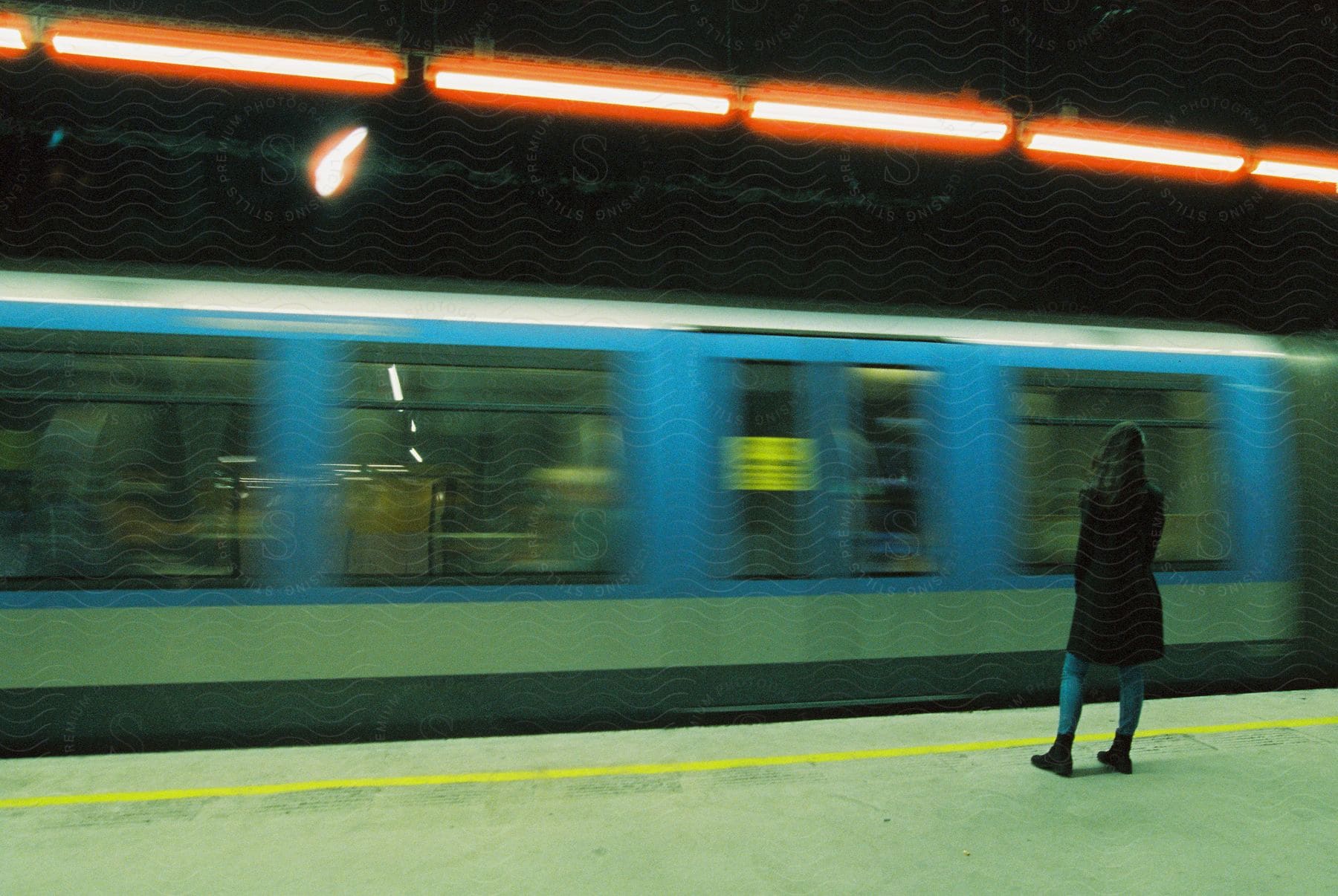 Woman standing on subway platform as train drives by at night creating blurred motion