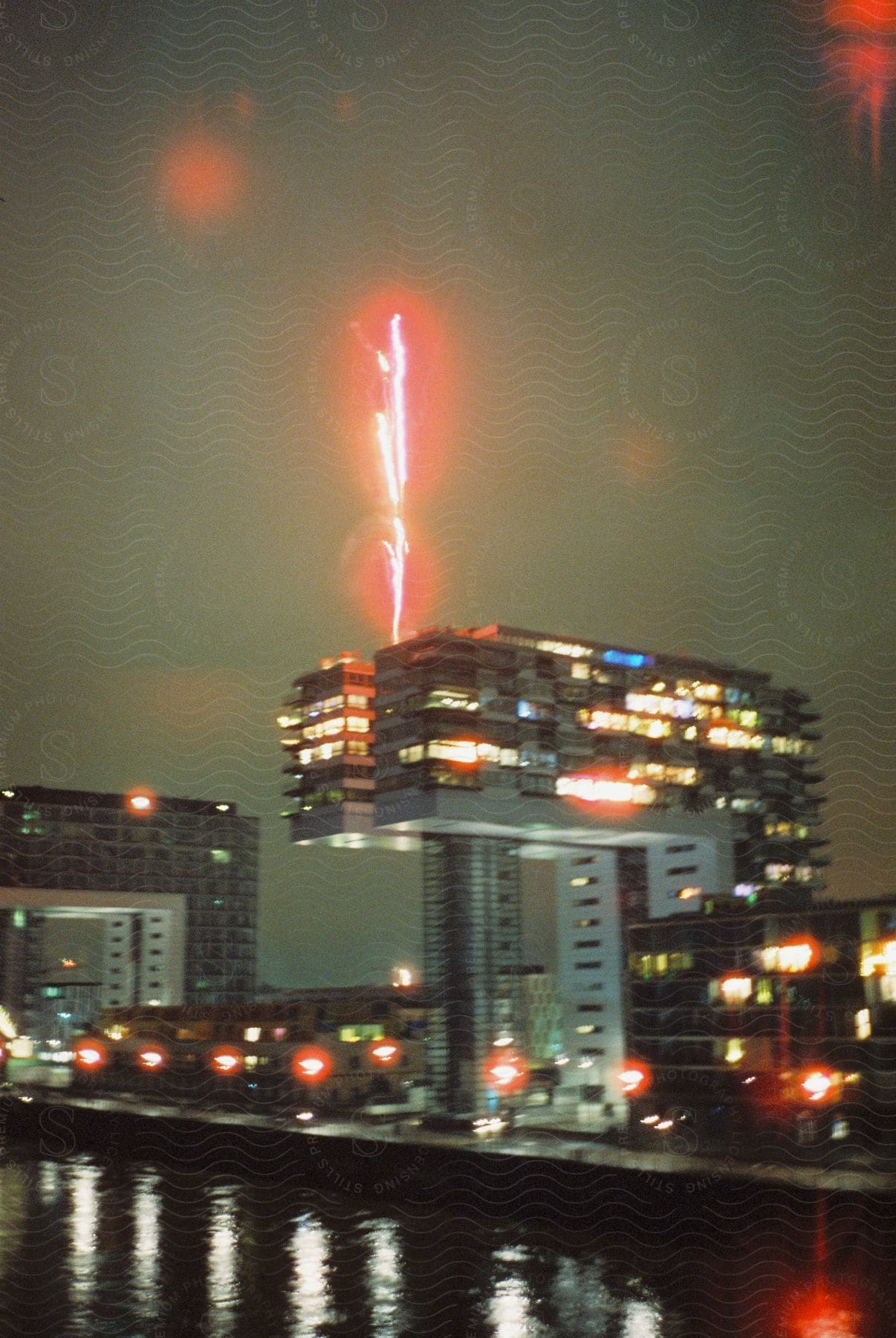 Modern buildings with lights on one building has a pink fireworklike line shooting out of the top