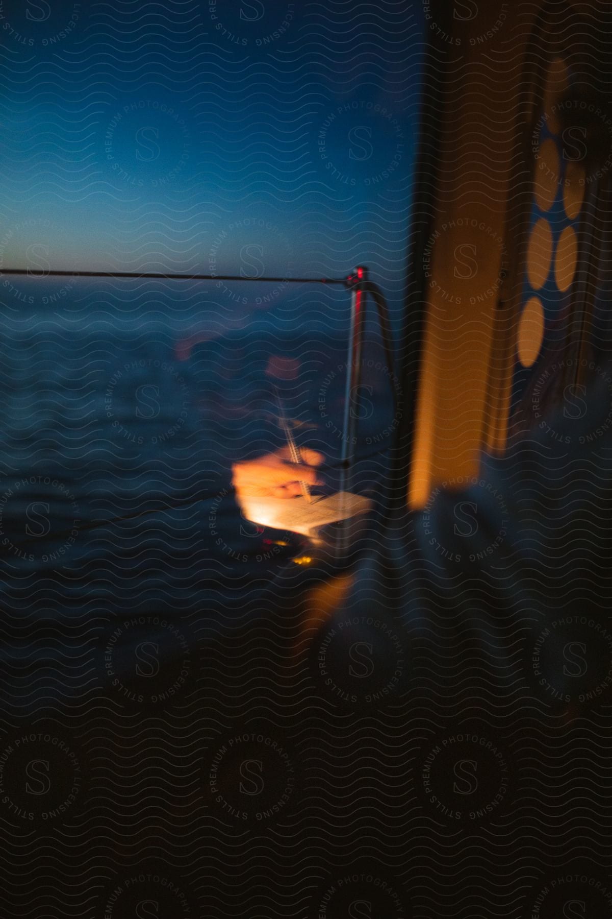 A person writes by candlelight on a boat at dusk