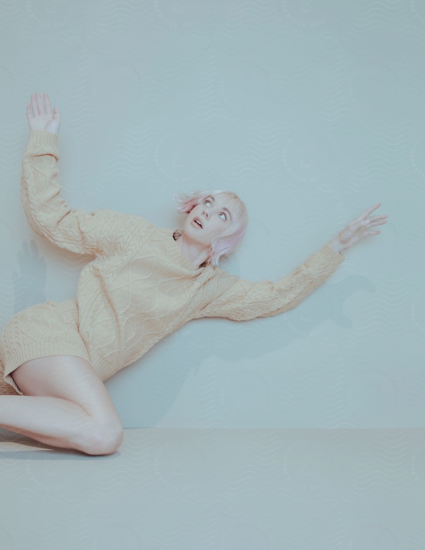 A young woman with pink hair poses for a photo against a blue background