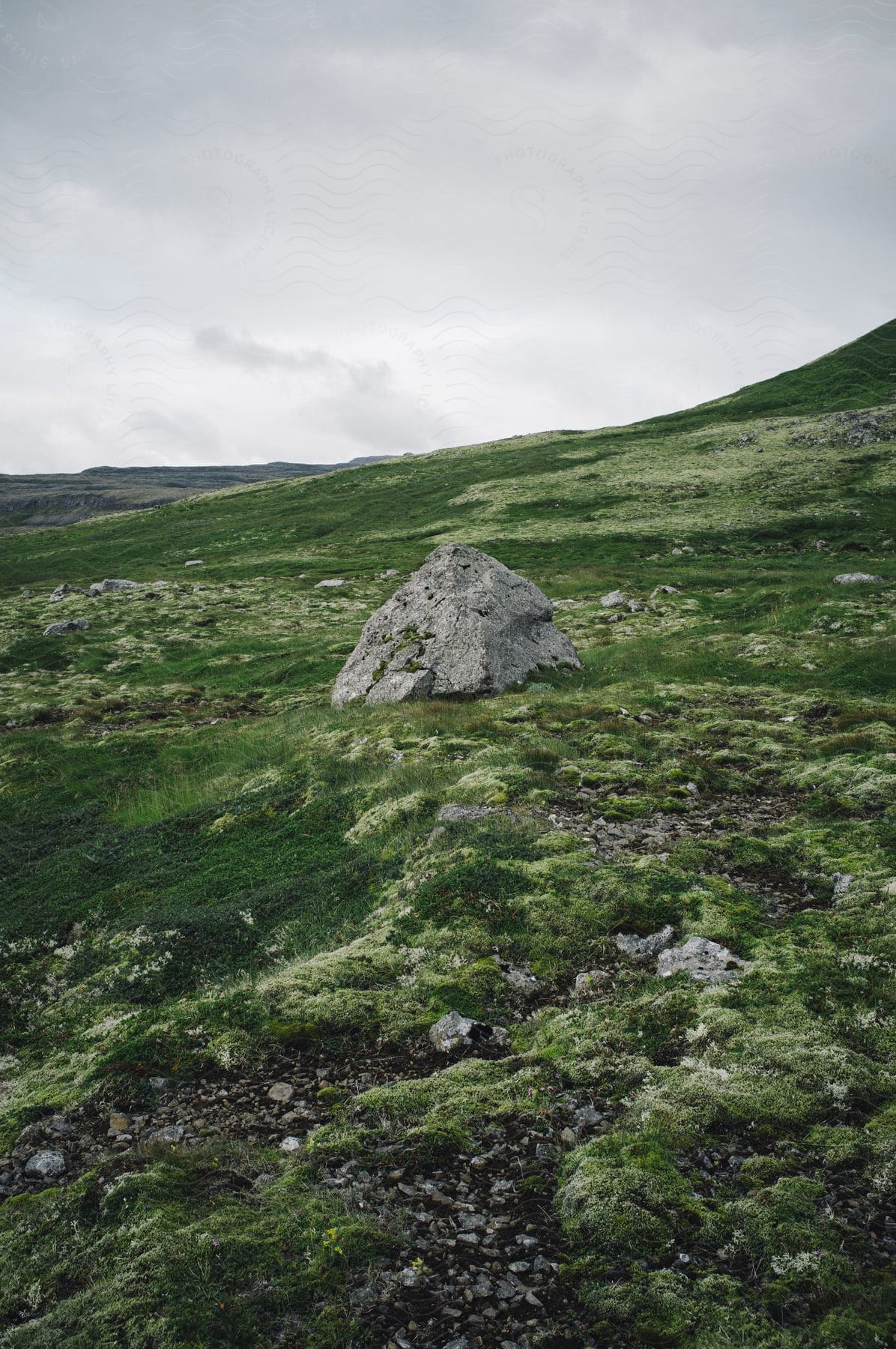 A rock sits on a grassy plain with hills in the background