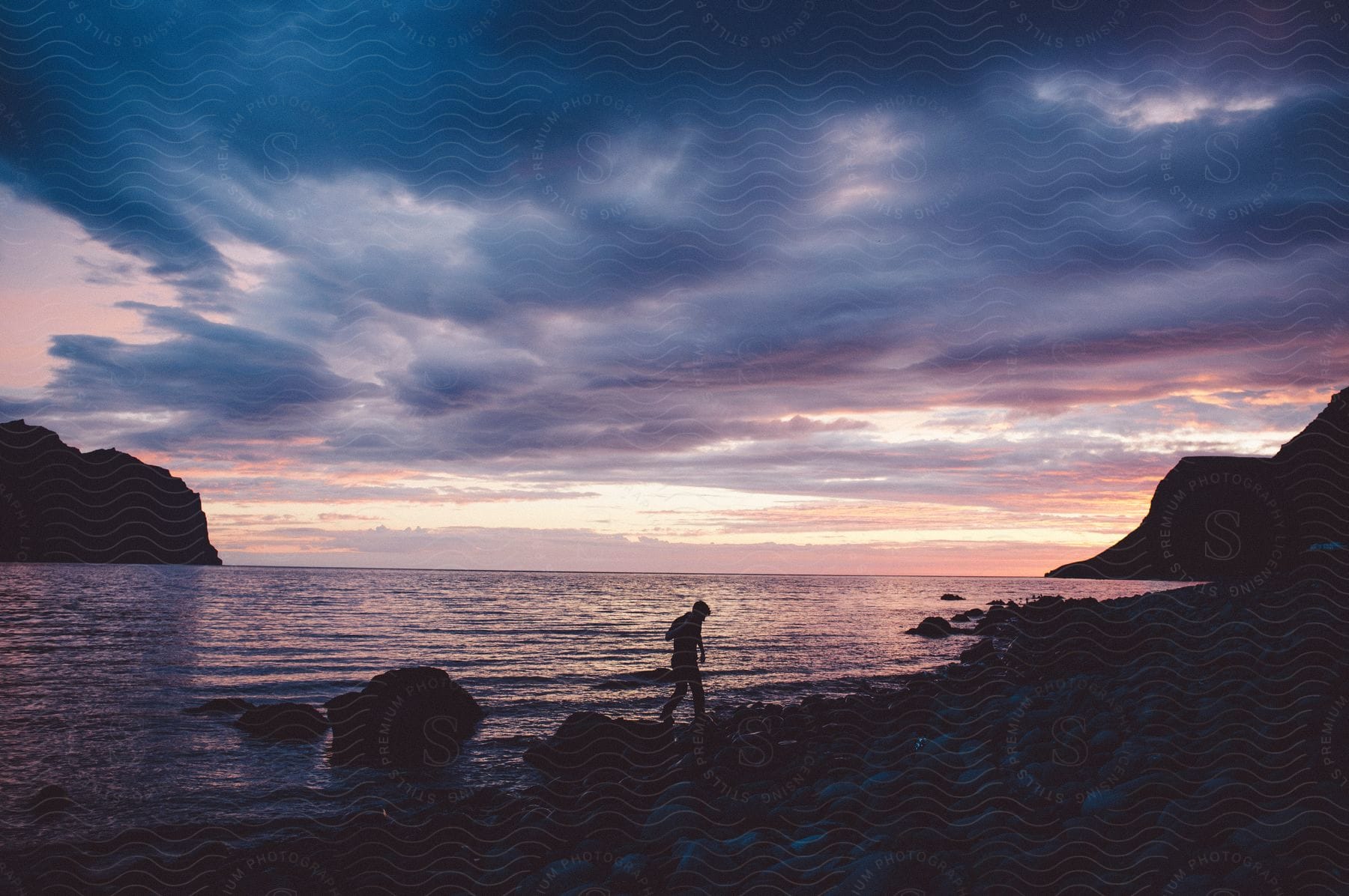 A person walking along a rocky ocean shoreline at dawn