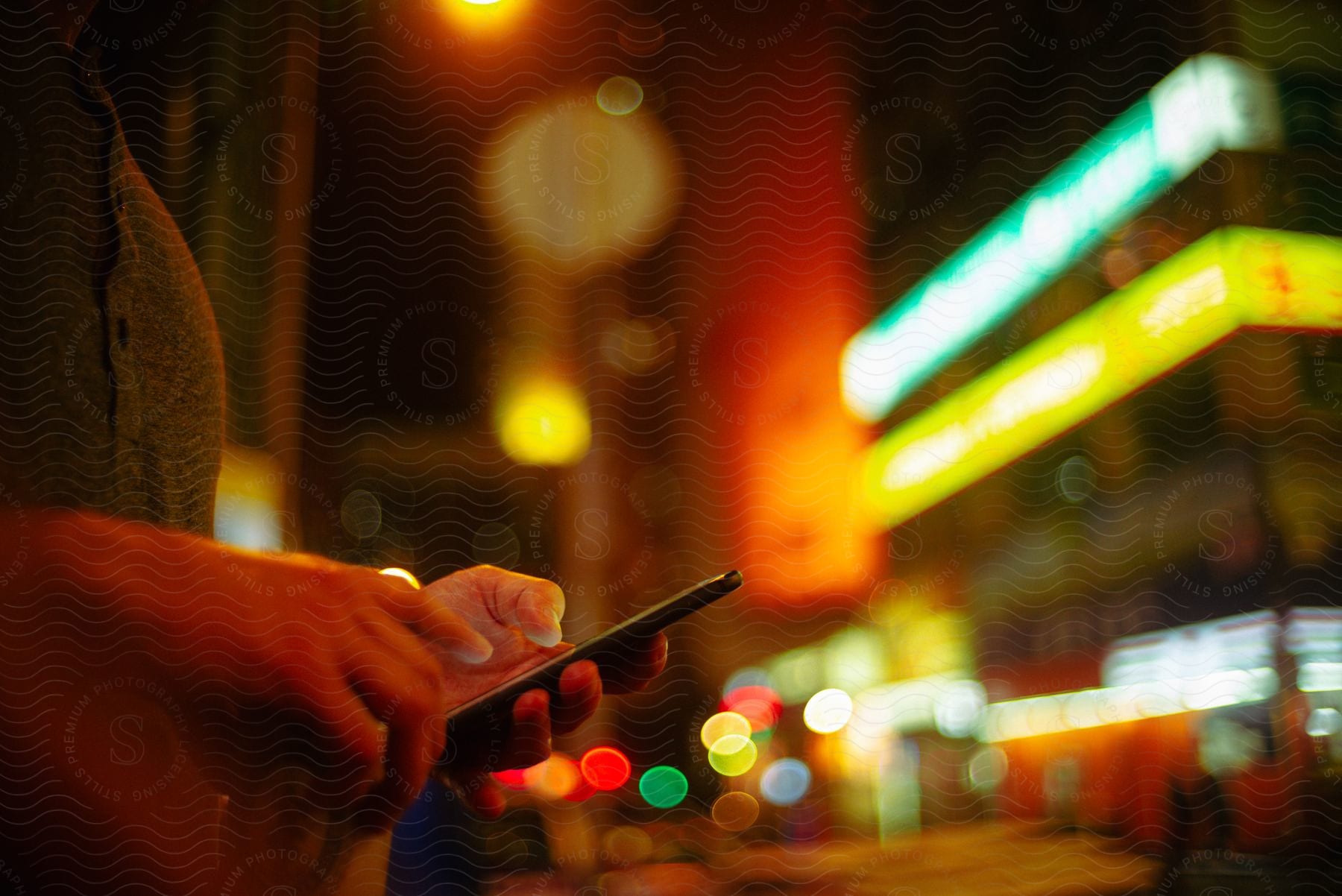 Person holding a cell phone on a street with brightly lit buildings