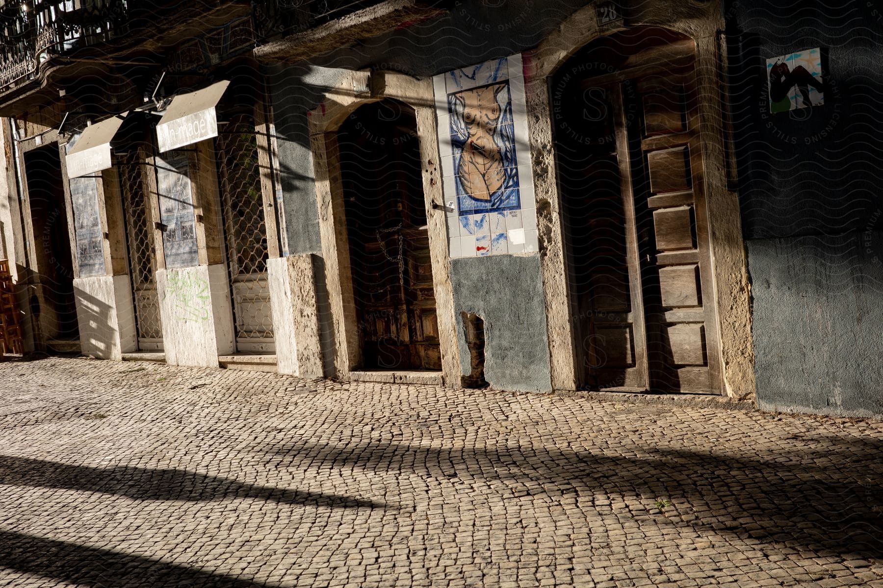 Shadows cast across a cobblestone street with wooden doorways and paintings on the walls in lisbon