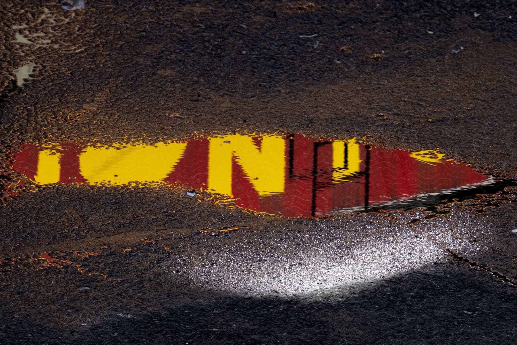 An abstract artwork of a concrete ground with a puddle reflecting something red with yellow letters