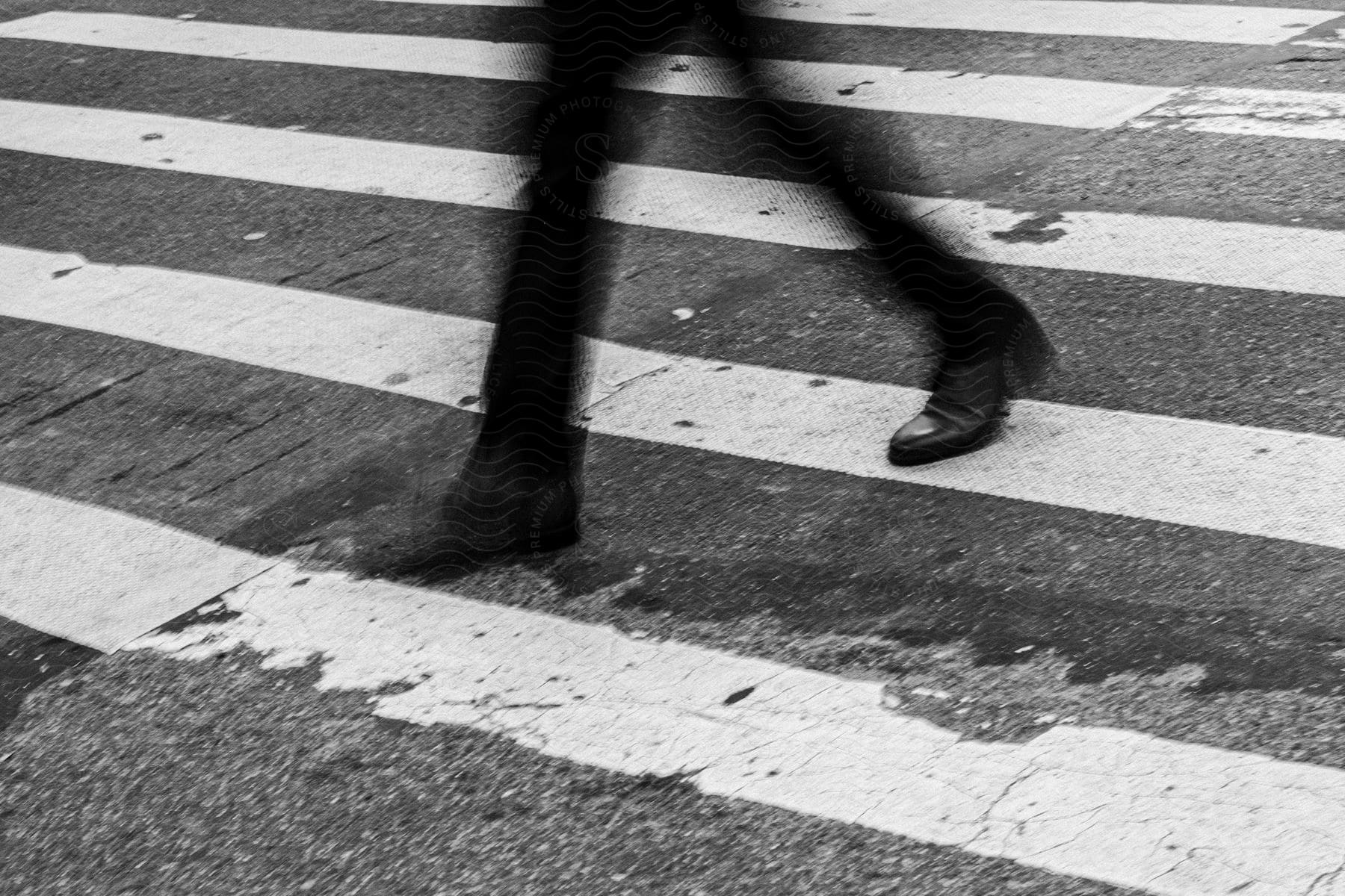 A person wearing black pants and shoes walks in a crosswalk