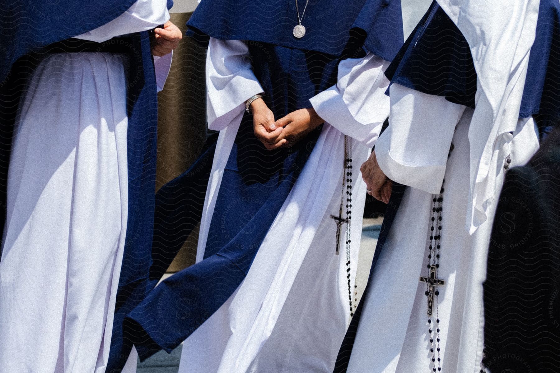 Three nuns with faces out of frame stand together hands folded wearing rosary beads