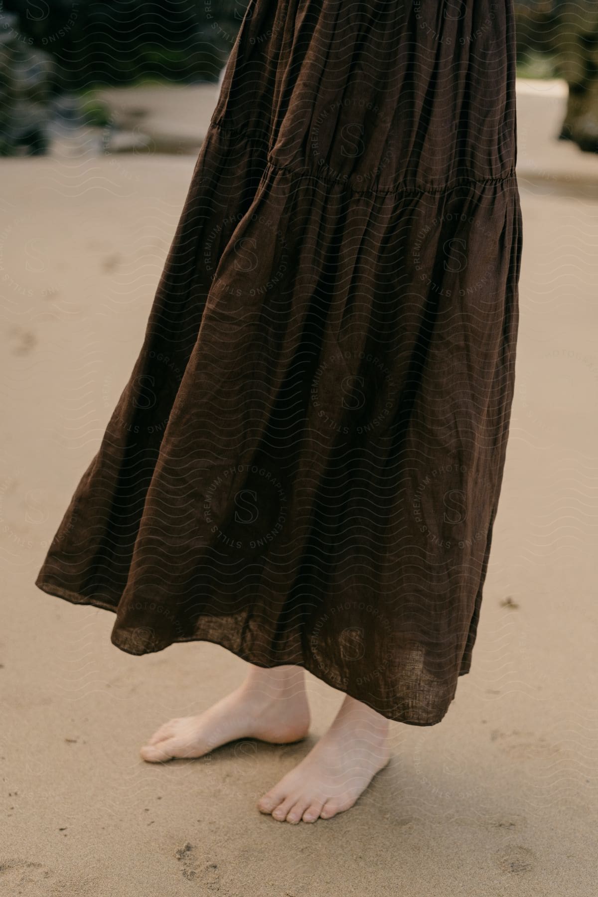 Woman in long brown skirt standing barefoot on sand beach