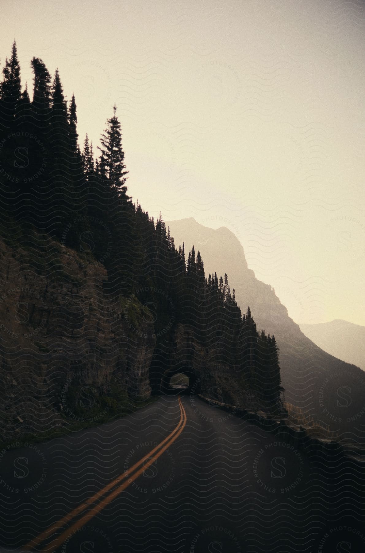 A highway runs through a forested mountain road with mountains in the distance under a hazy sky