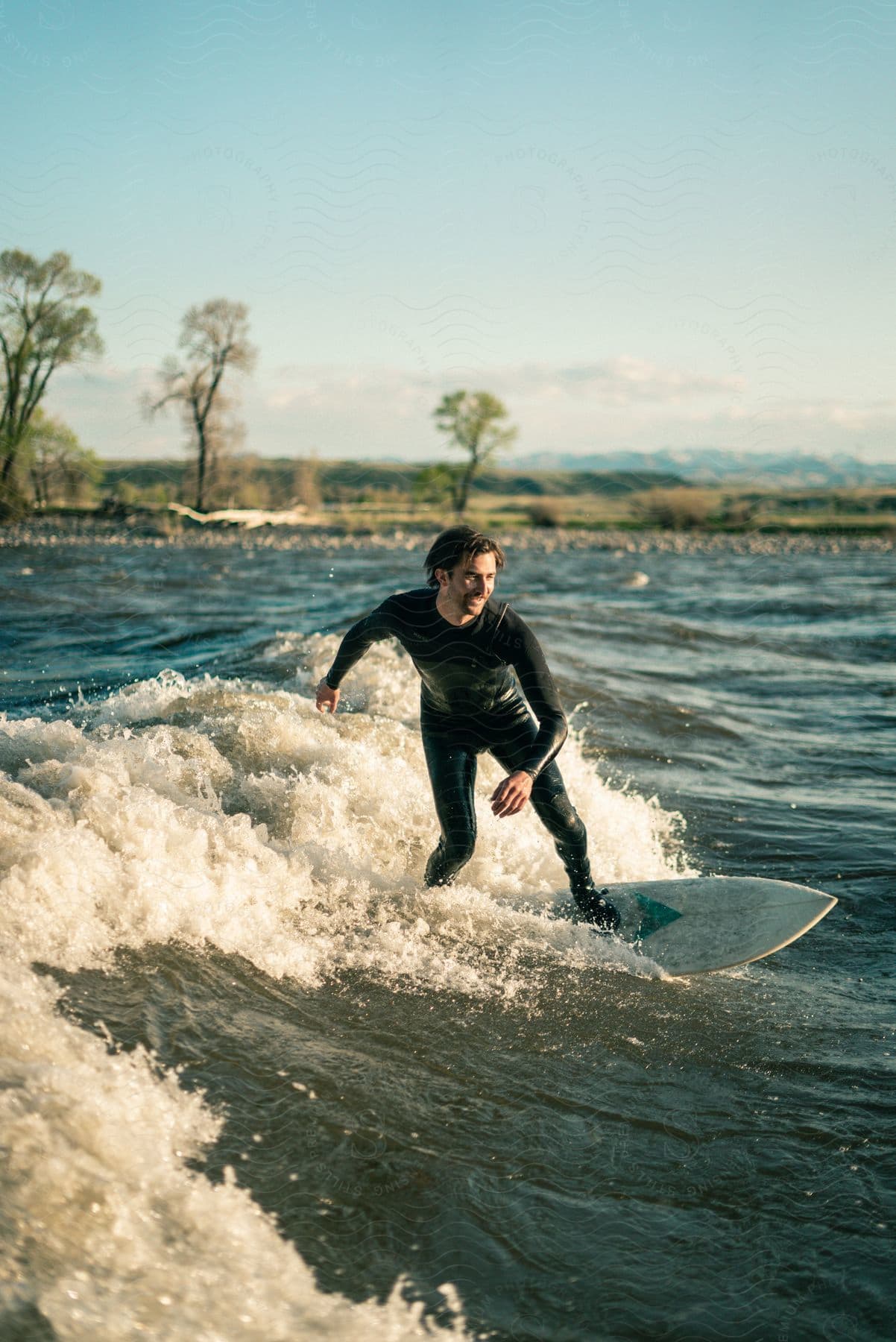 A happy man wearing a wetsuit is surfing a small wave on a sunny day