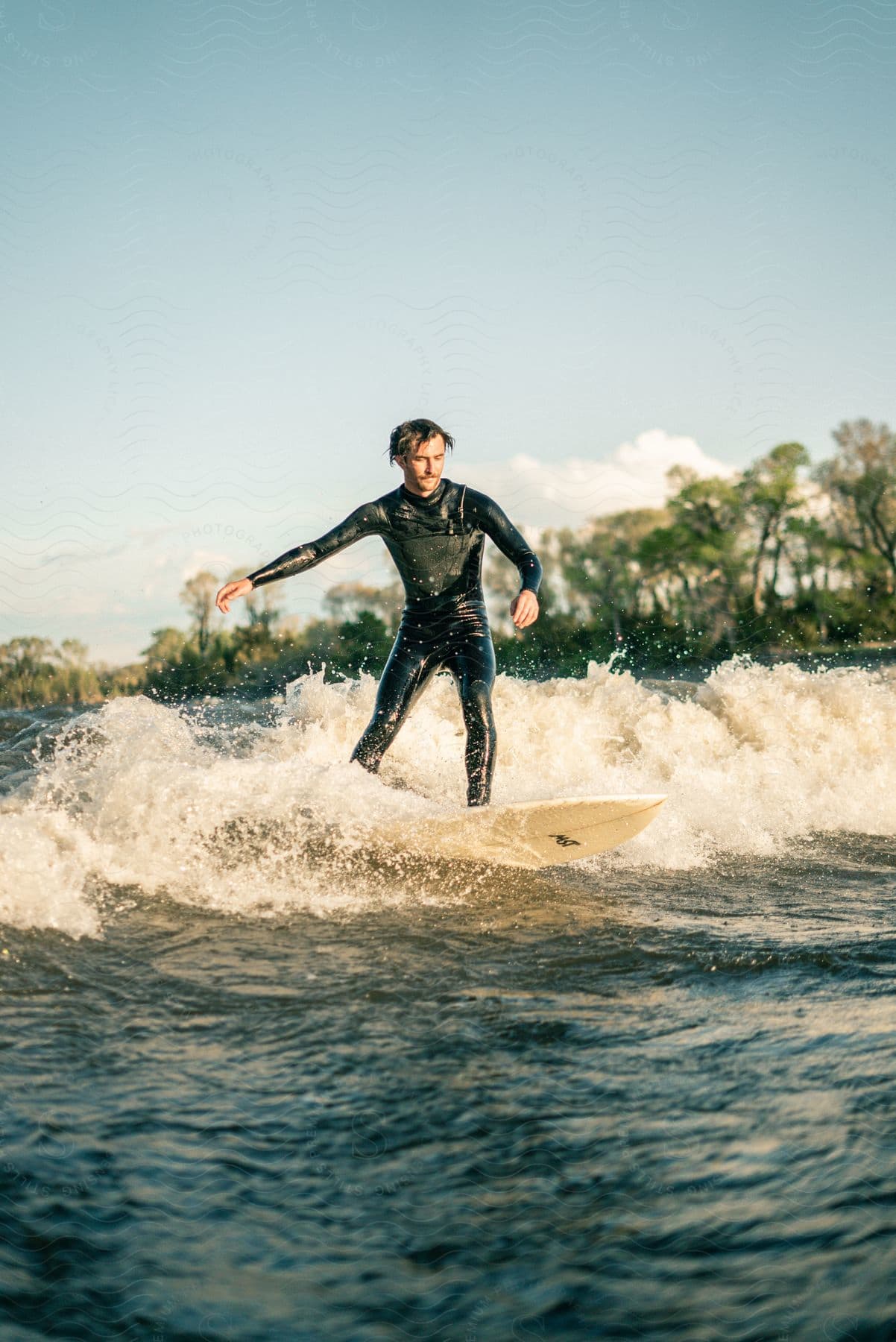 A man in a wetsuit rides a small wave on a sunny day while river surfing in montana at dusk