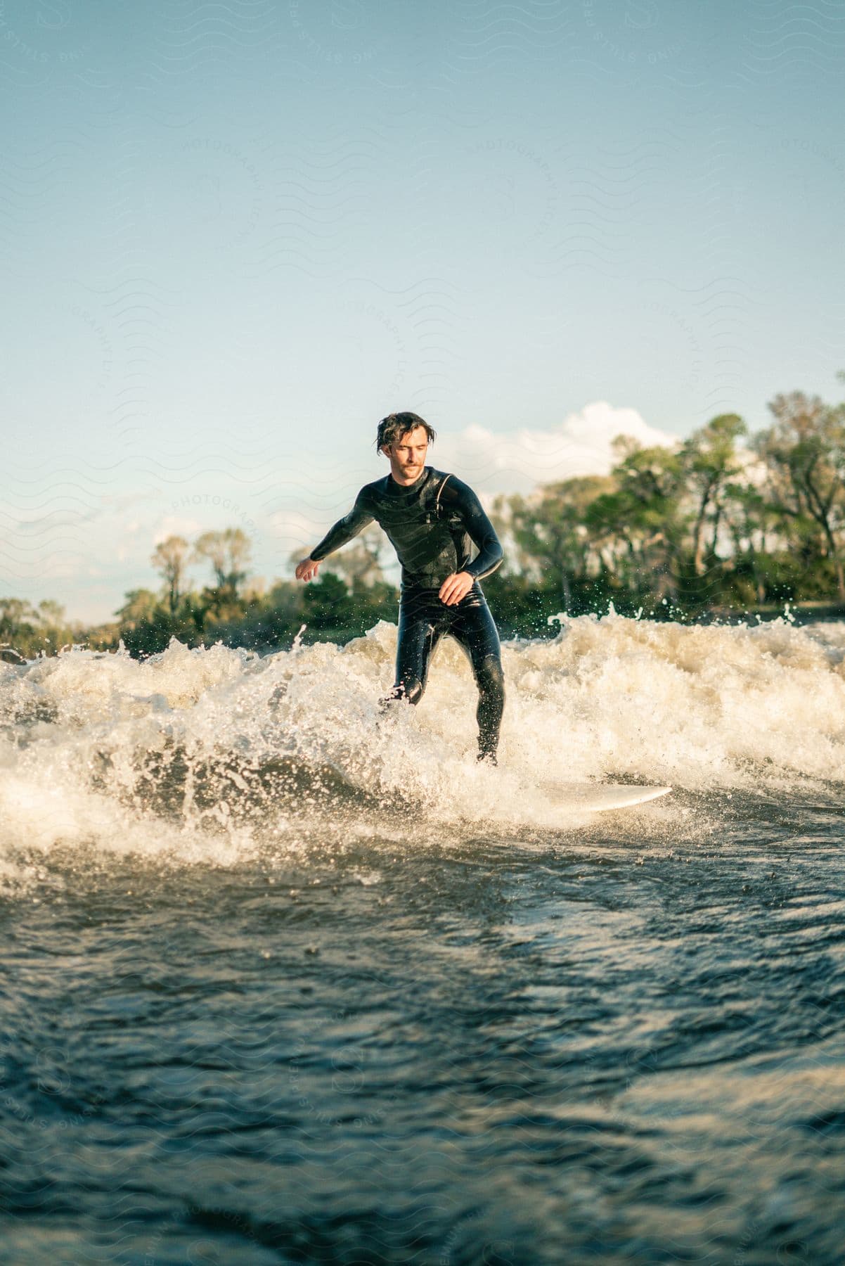 A man wearing a wetsuit surfing a small wave on a sunny day in nature
