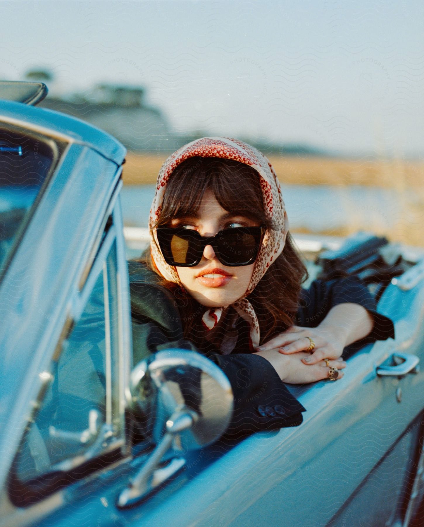 A woman in sunglasses leans out of a blue convertible