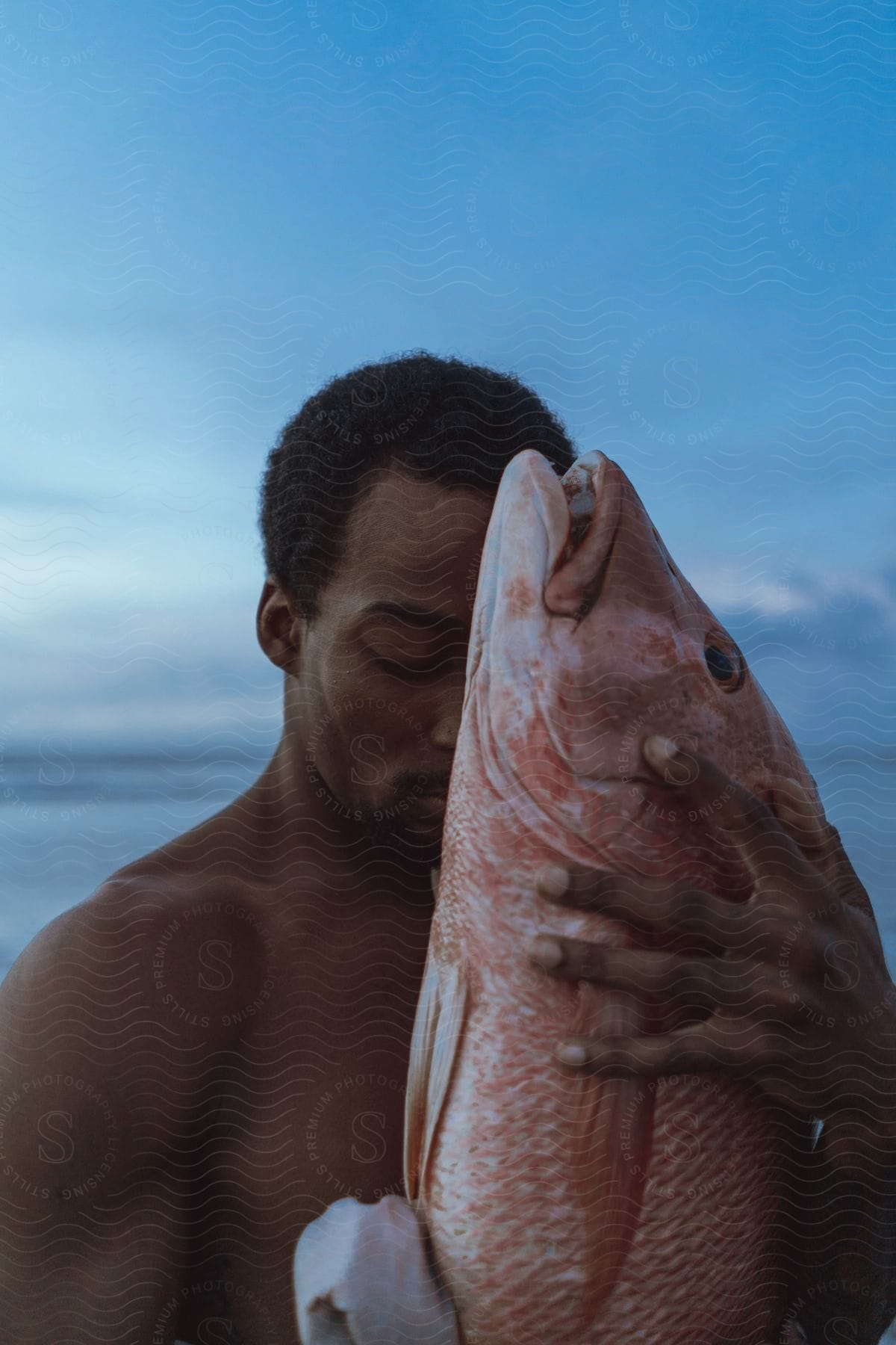 A Man Stands With A Large Fish Obscuring Half Of His Face