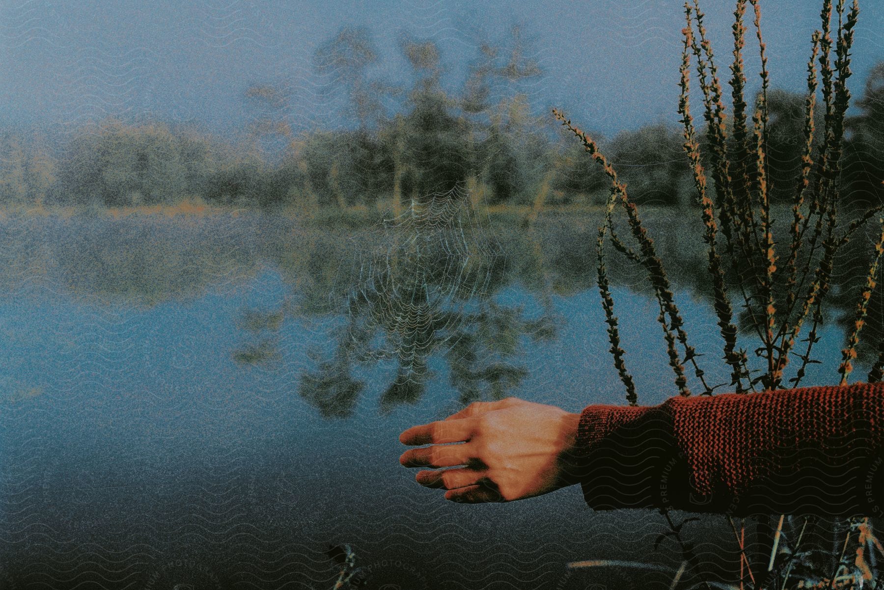 A persons hand is outdoors by the lake in the day time