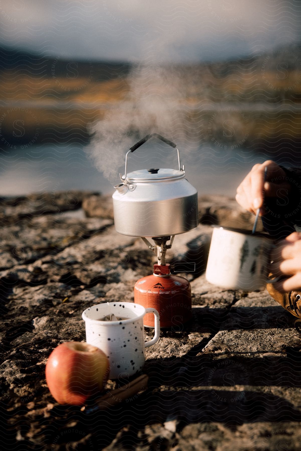 A person boils water to make tea near the shore of a lake