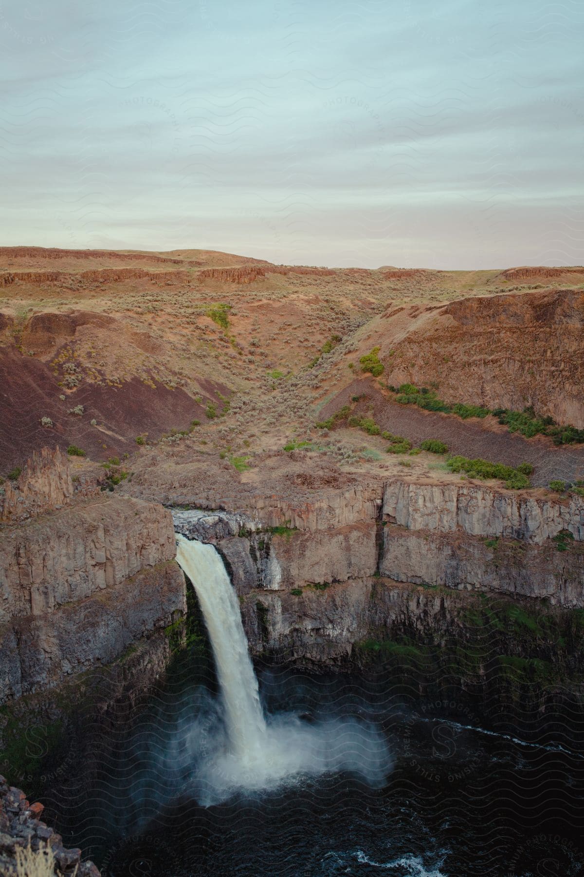 Aerial view of palouse falls waterfall plunging from basalt rockwall into roaring river under purple clouded sky