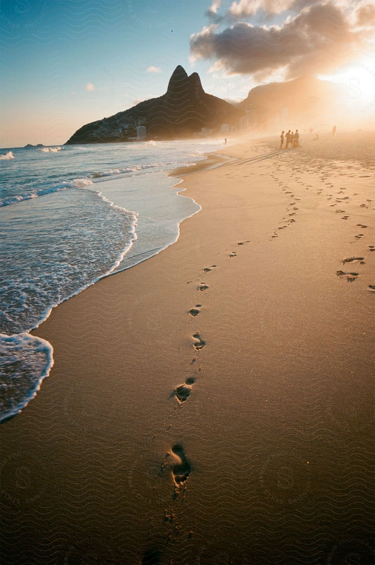 Footprints meander along ipanema beach at dusk with mountains rising at the end