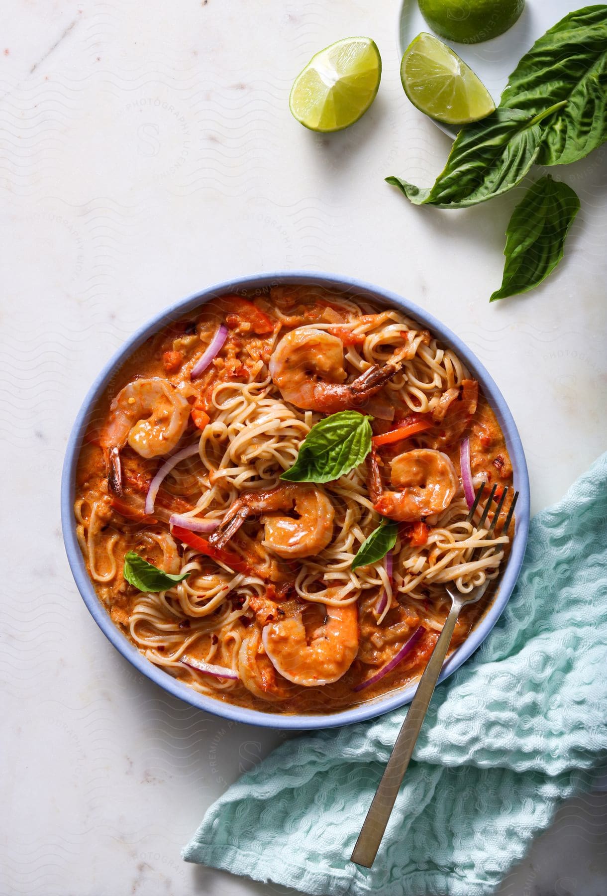 A shrimp and pasta bowl on a white kitchen table next to some limes and bay leaves