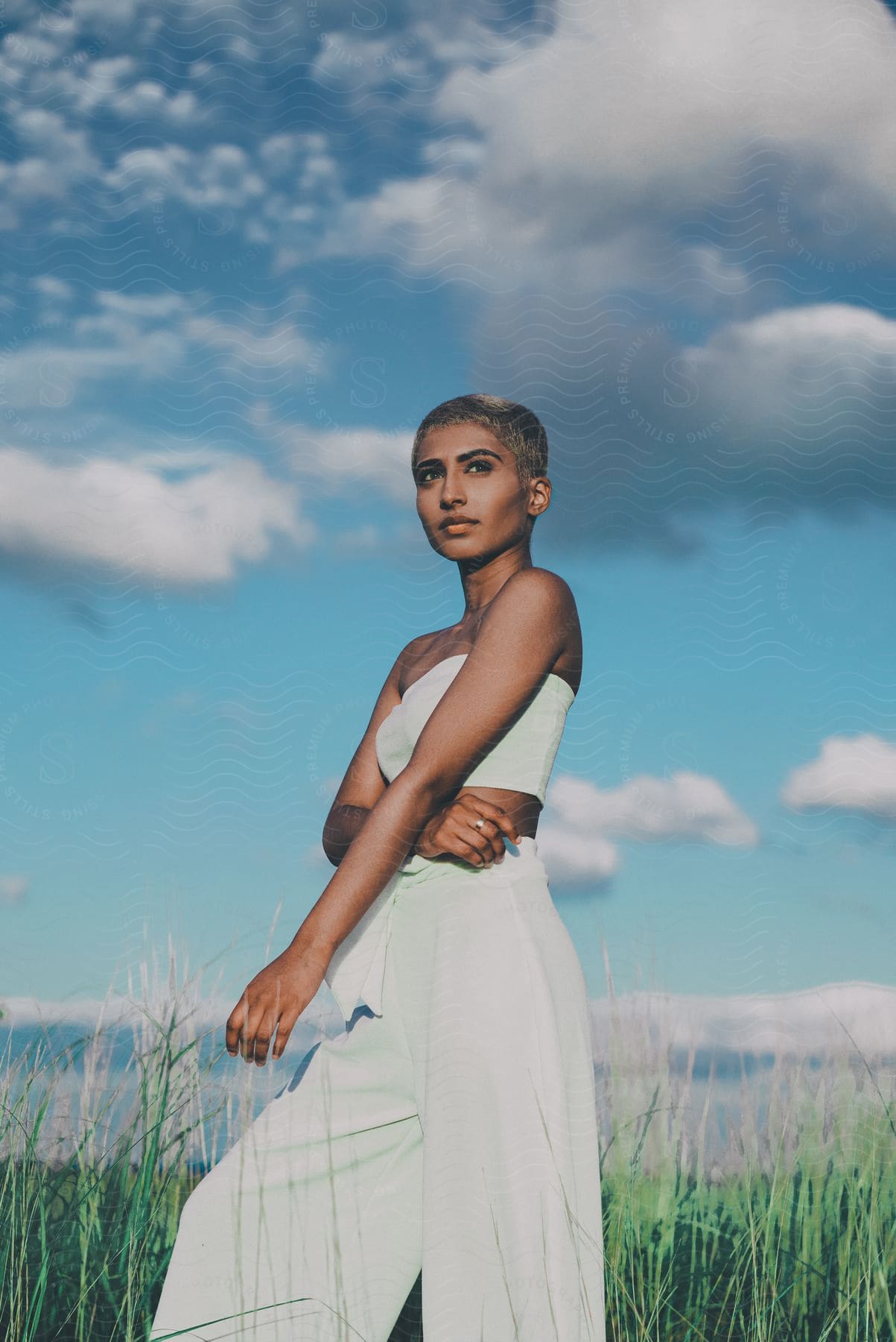 Stock photo of woman with short hair wearing white top and pants stands on grassland