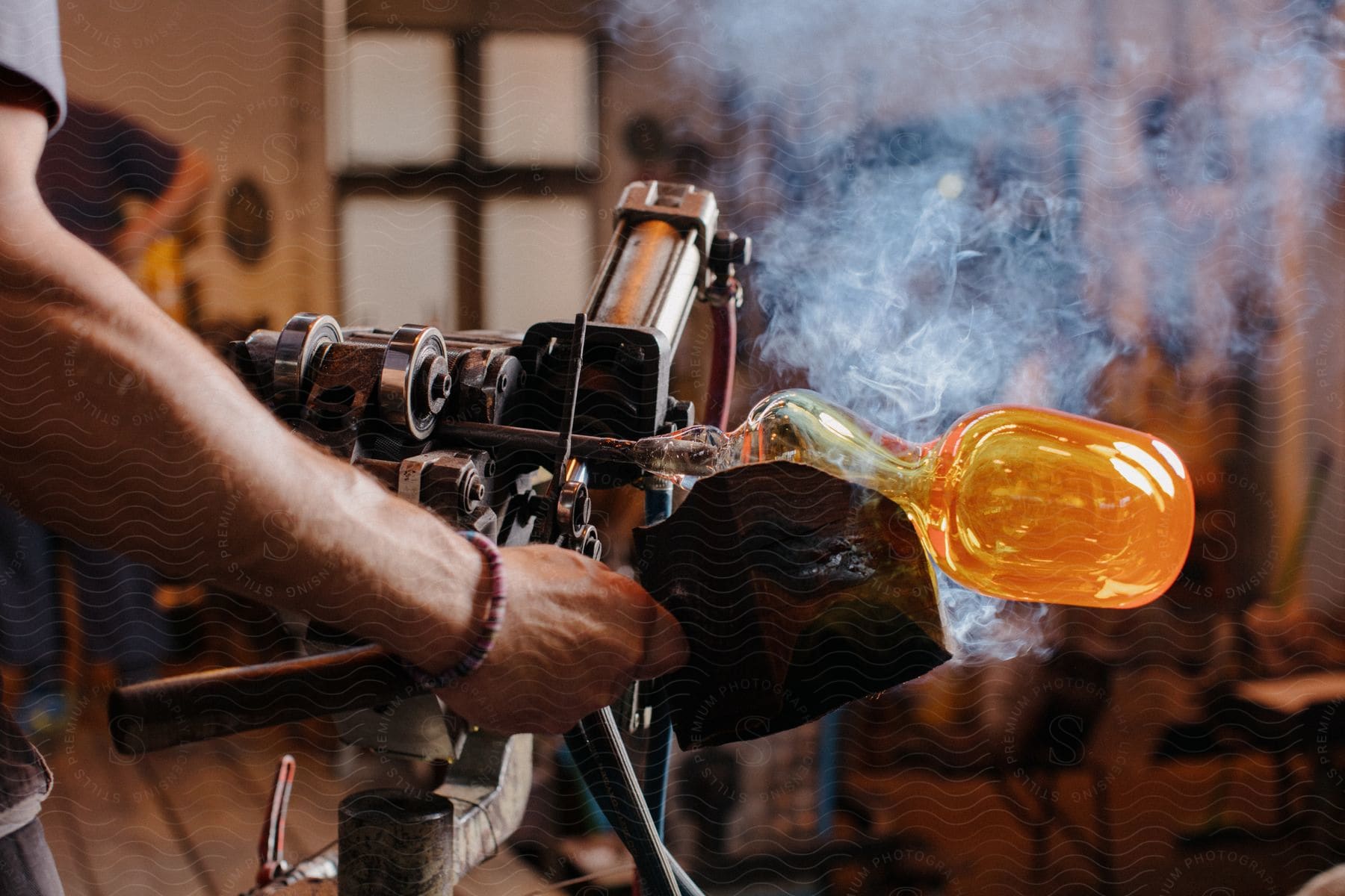 Stock photo of a man shapes hot glass as smoke rises in a factory building