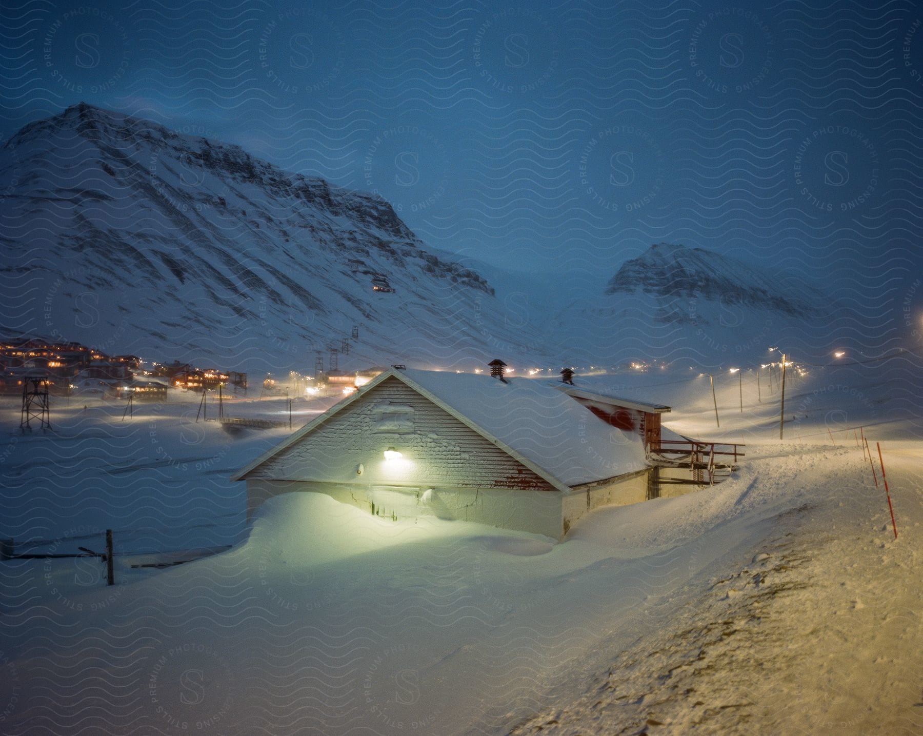 A snowcovered house in a small mountain town illuminated by street and house lights at night