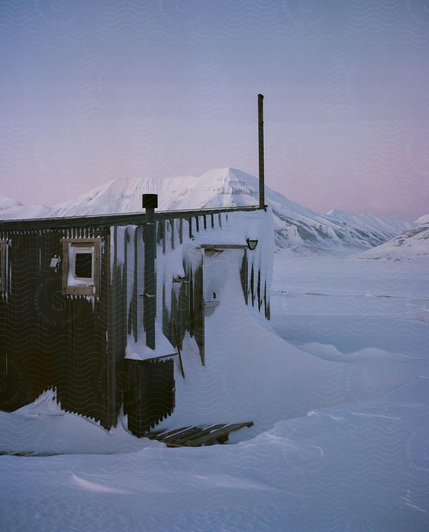 A snowy cabin near a frozen lake with a distant snowy mountain