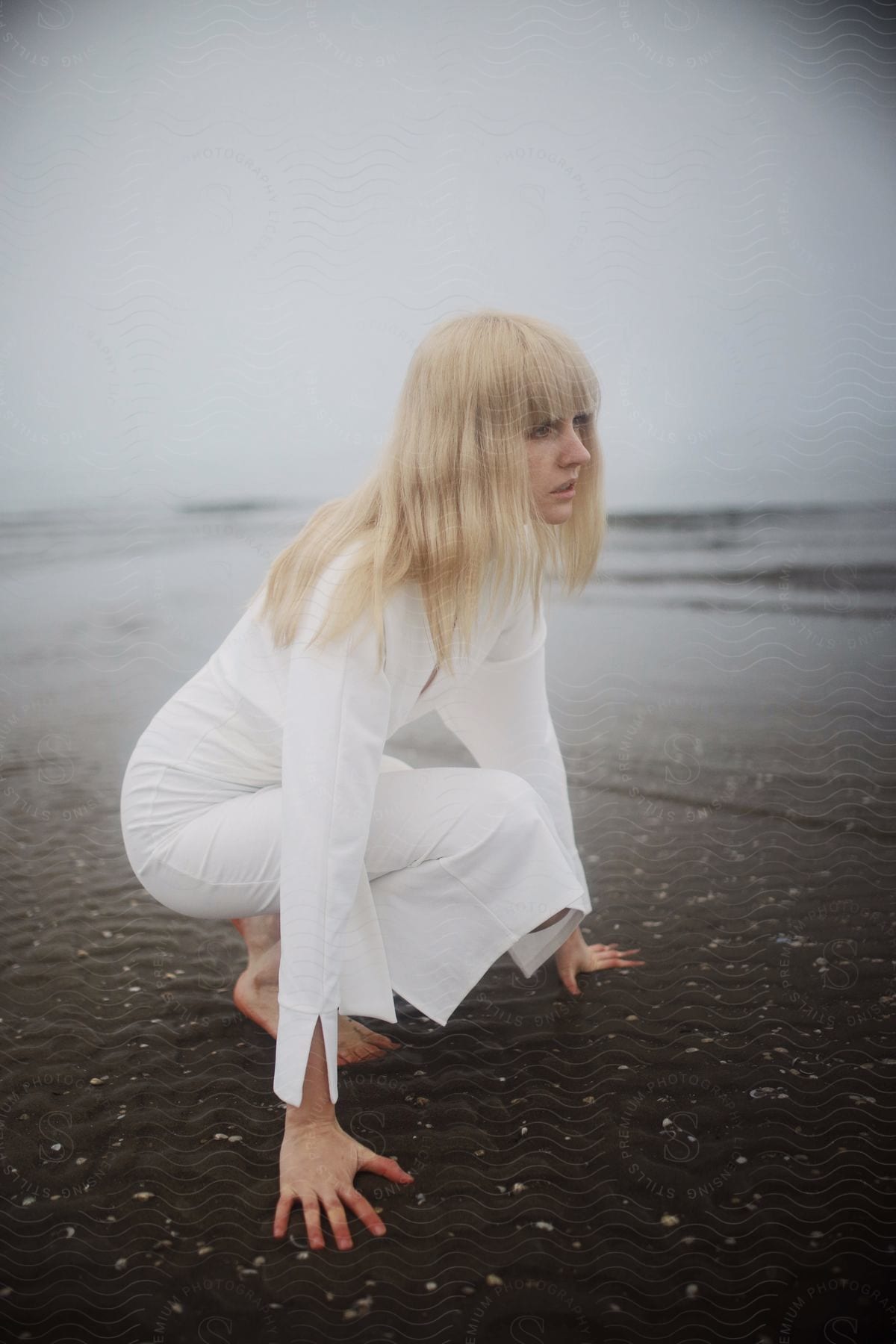 A woman in a white dress crouching on a cloudy beach