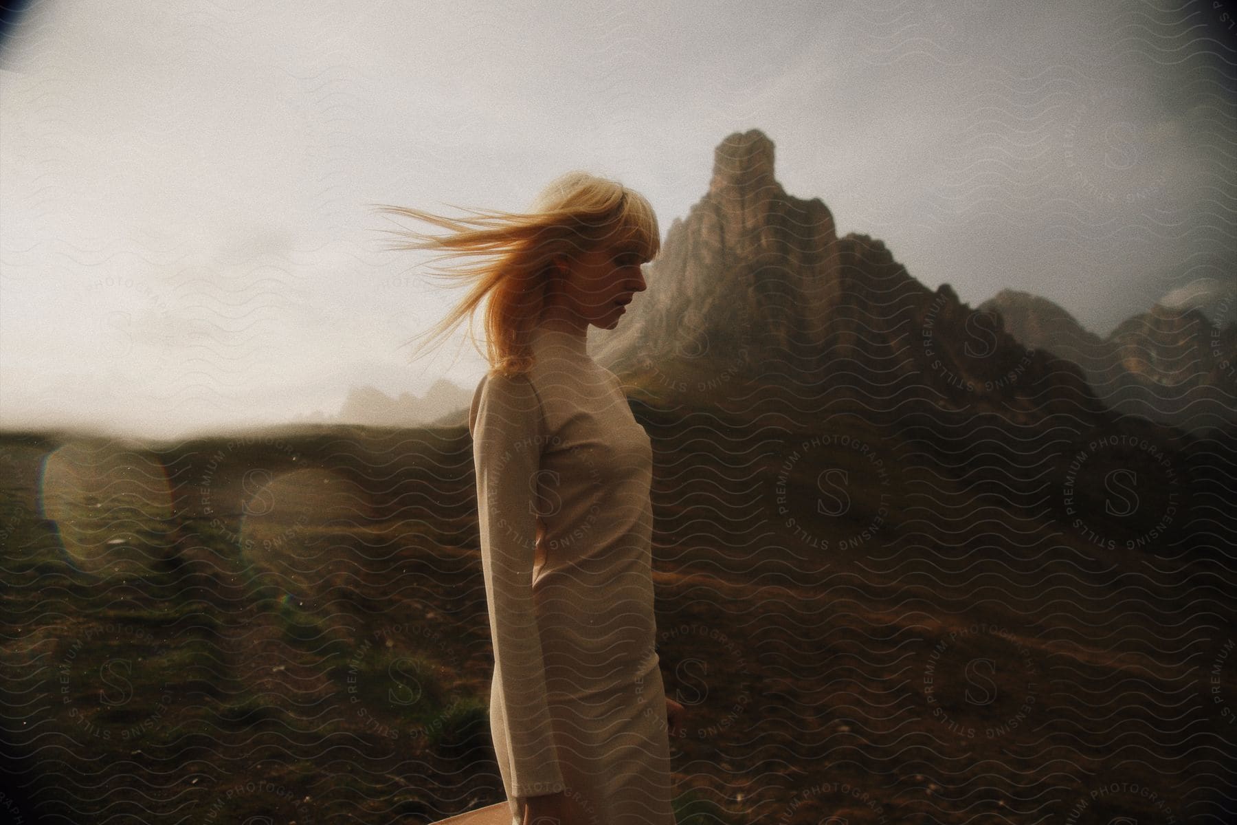 A woman in a white dress walks near a mountain on a windy day