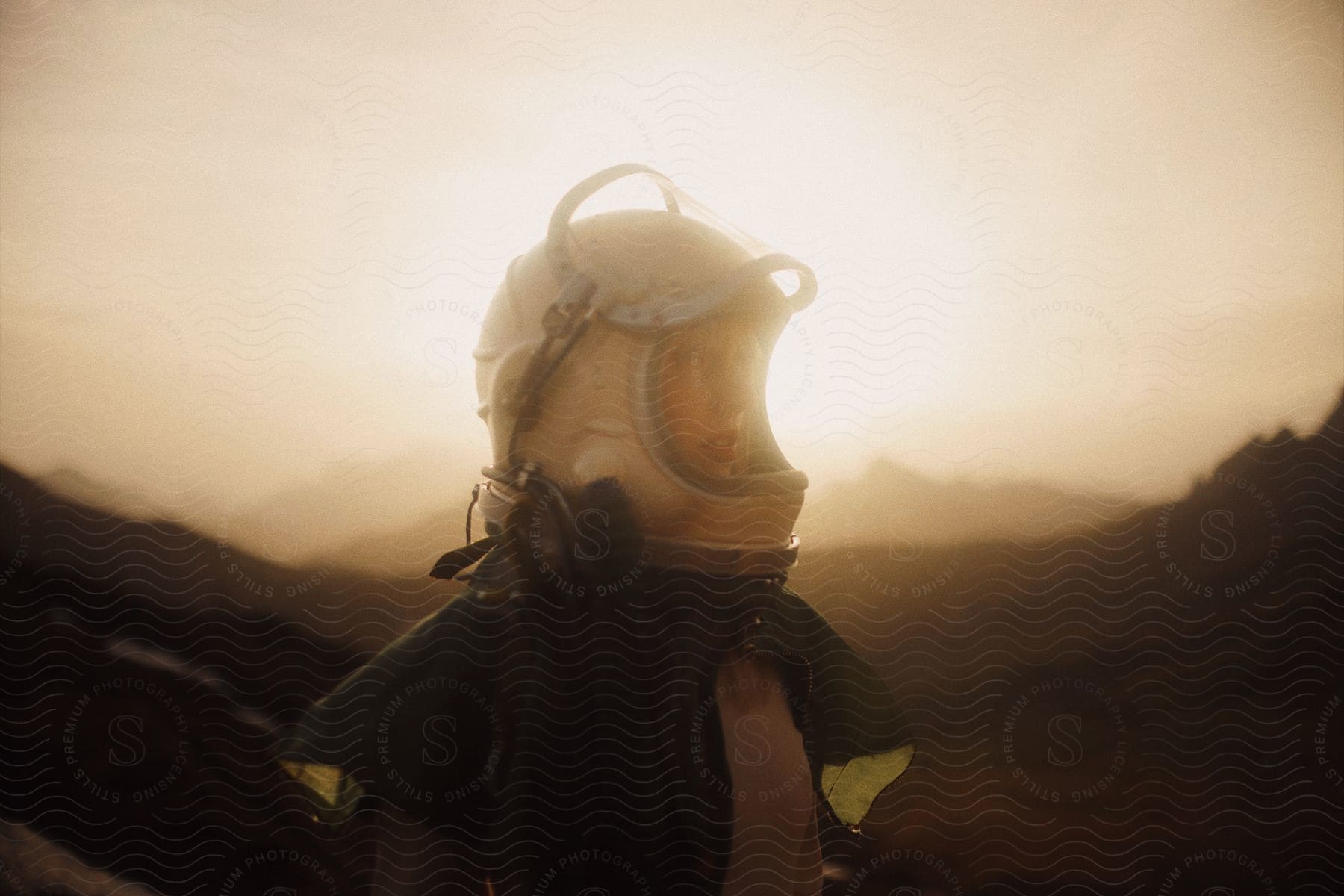 A woman in a motorcycle helmet looks to her left in front of hazy mountains