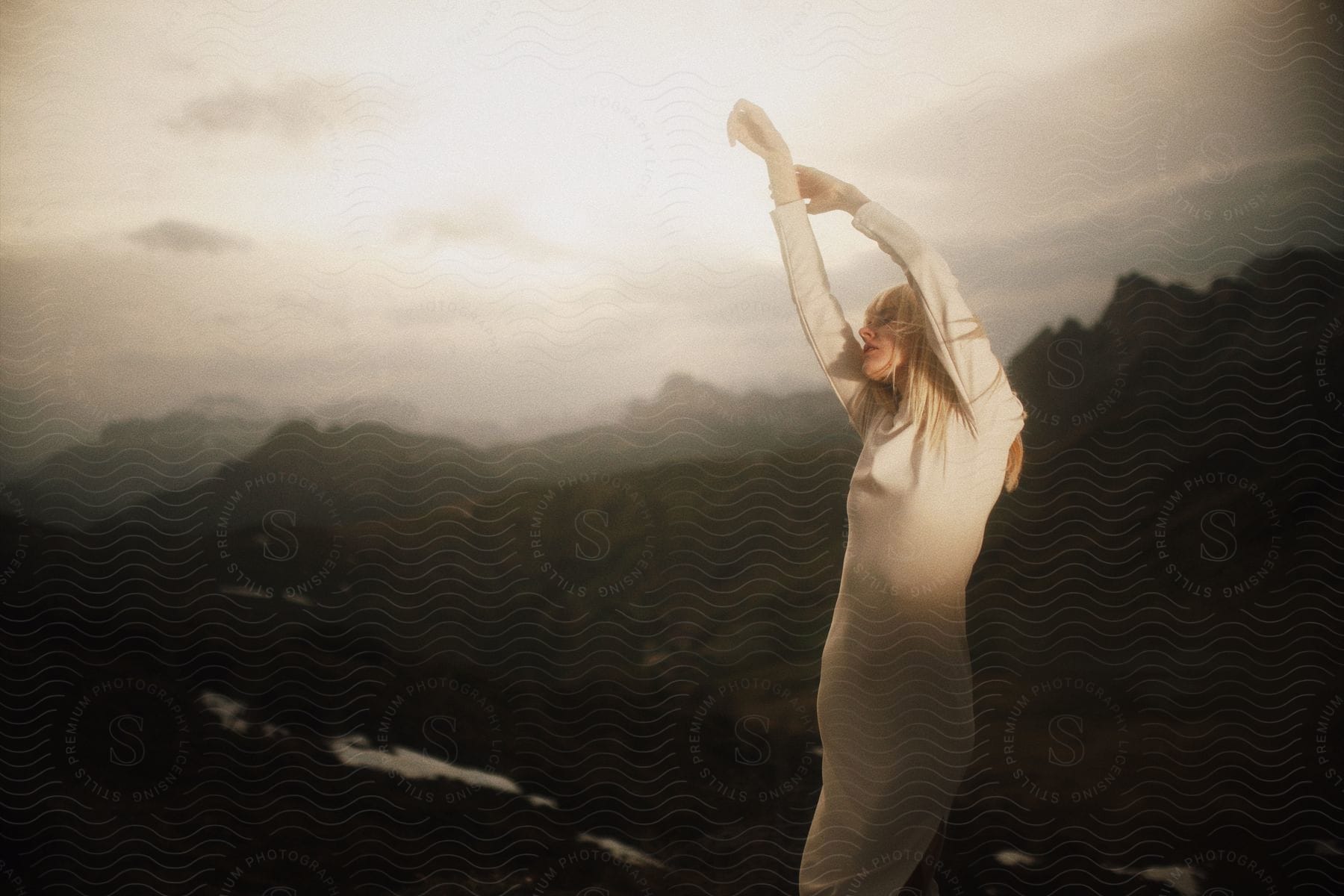 A woman stretches her arms in front of a mountain range and river