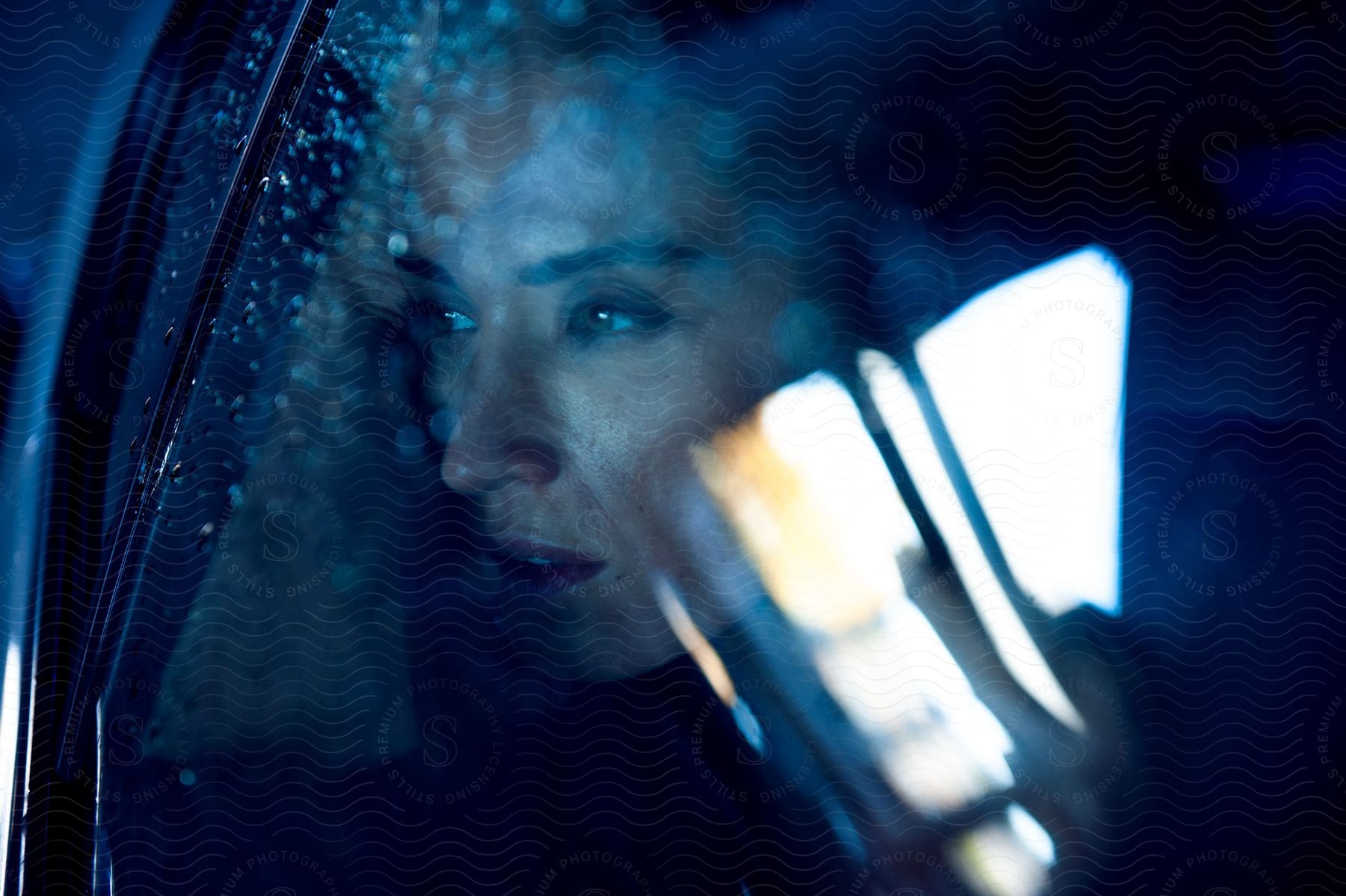 Woman inside car observing raindrops on window