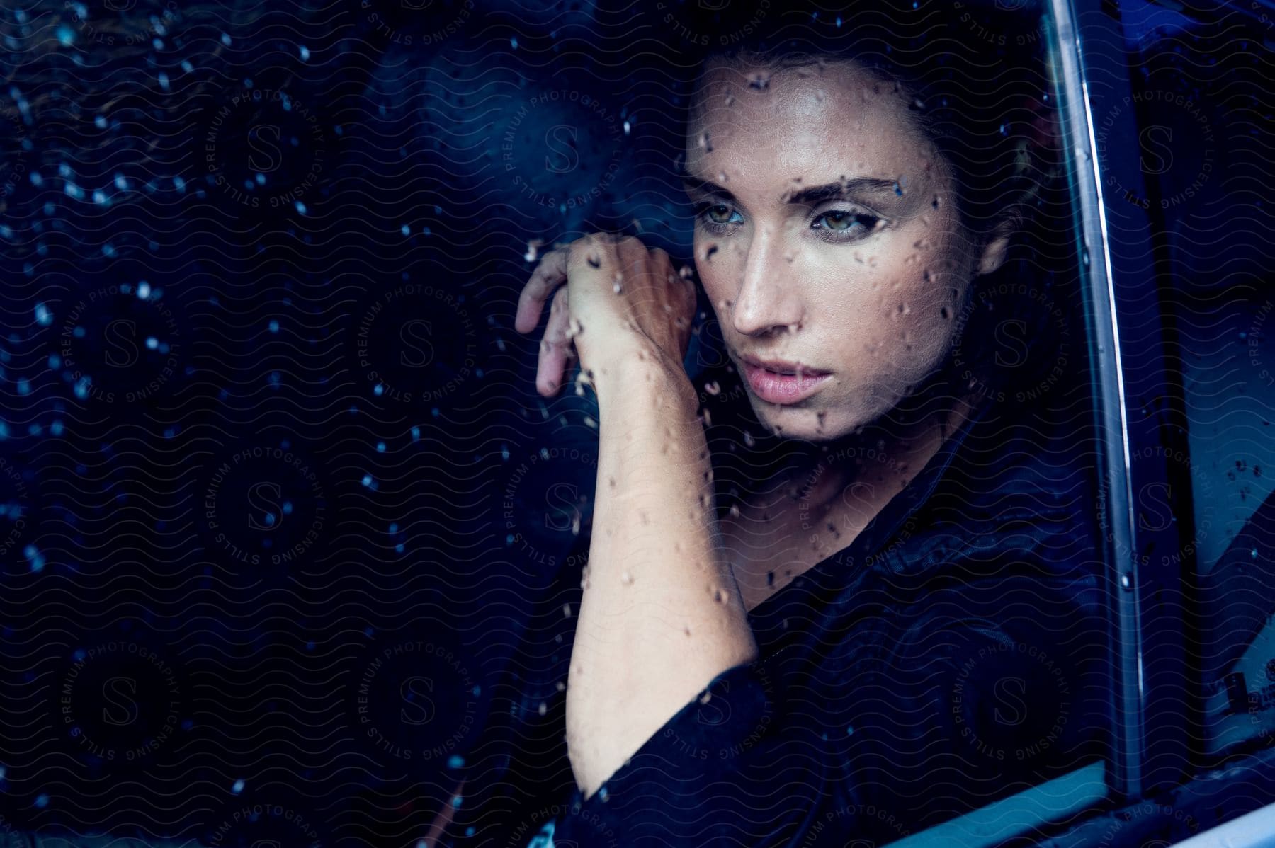 A person with black hair looking sad against a rainy car window