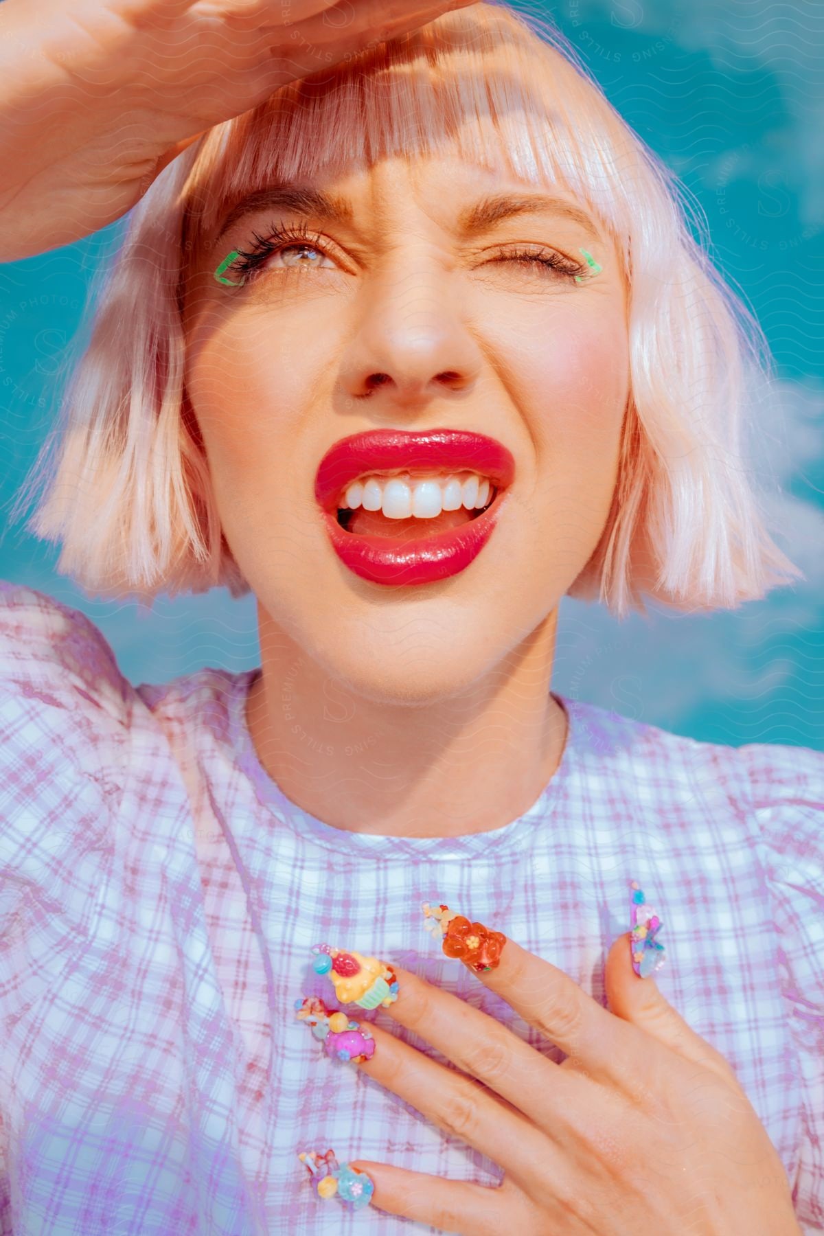 Blonde woman with red lips and flower manicure shading her forehead outside