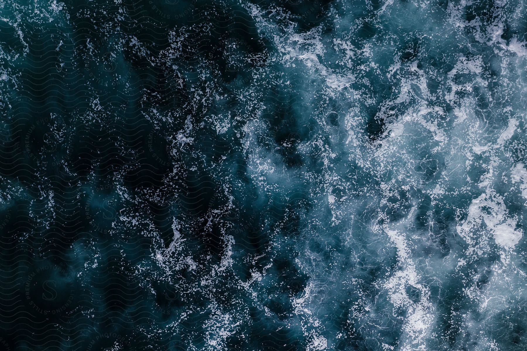 aerial view of ocean waves, with white foam on the surface of the blue water.