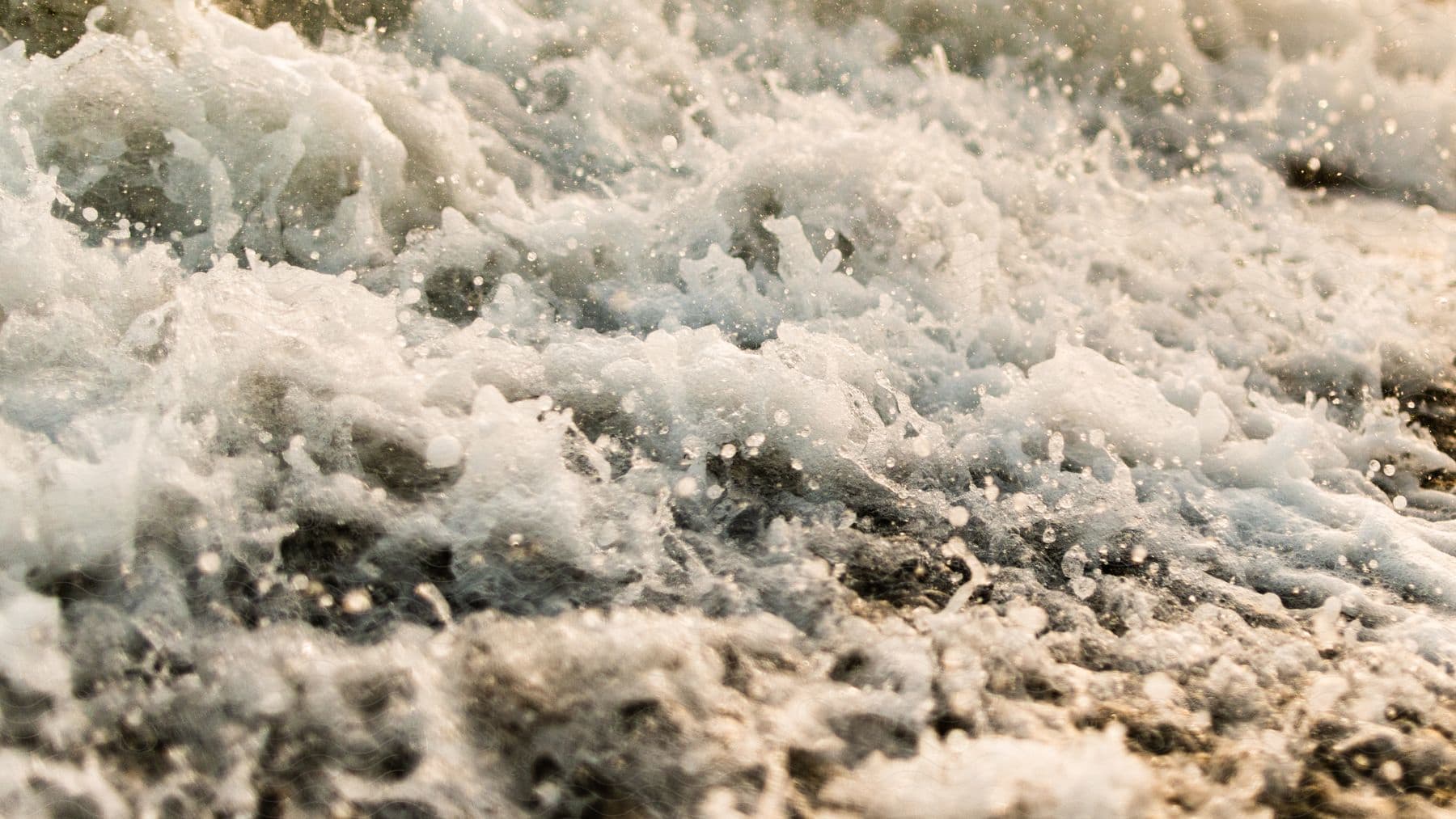 A wave splashing and creating foam on the beach.