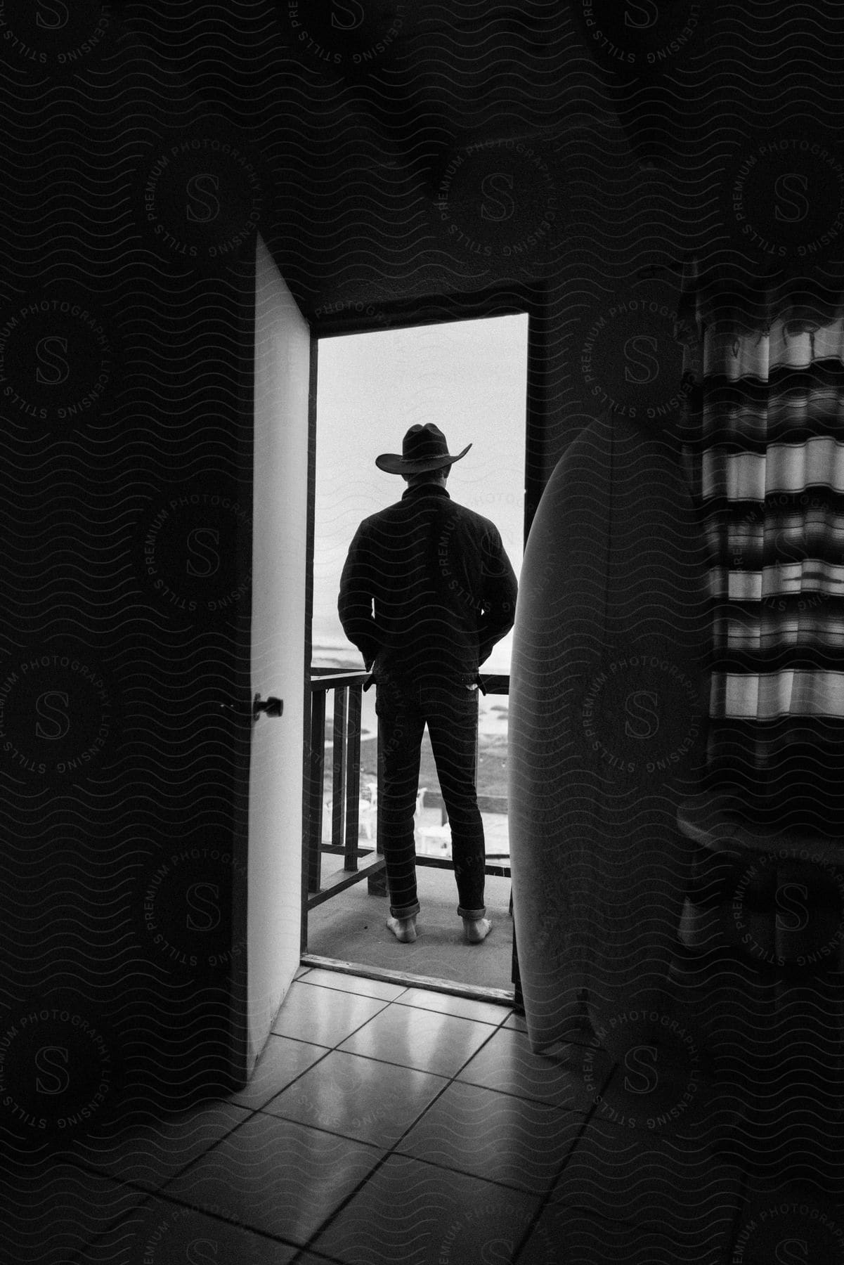 A rugged man, donned in a jacket and a worn cowboy hat, stands tall on the wooden porch, surveying the horizon