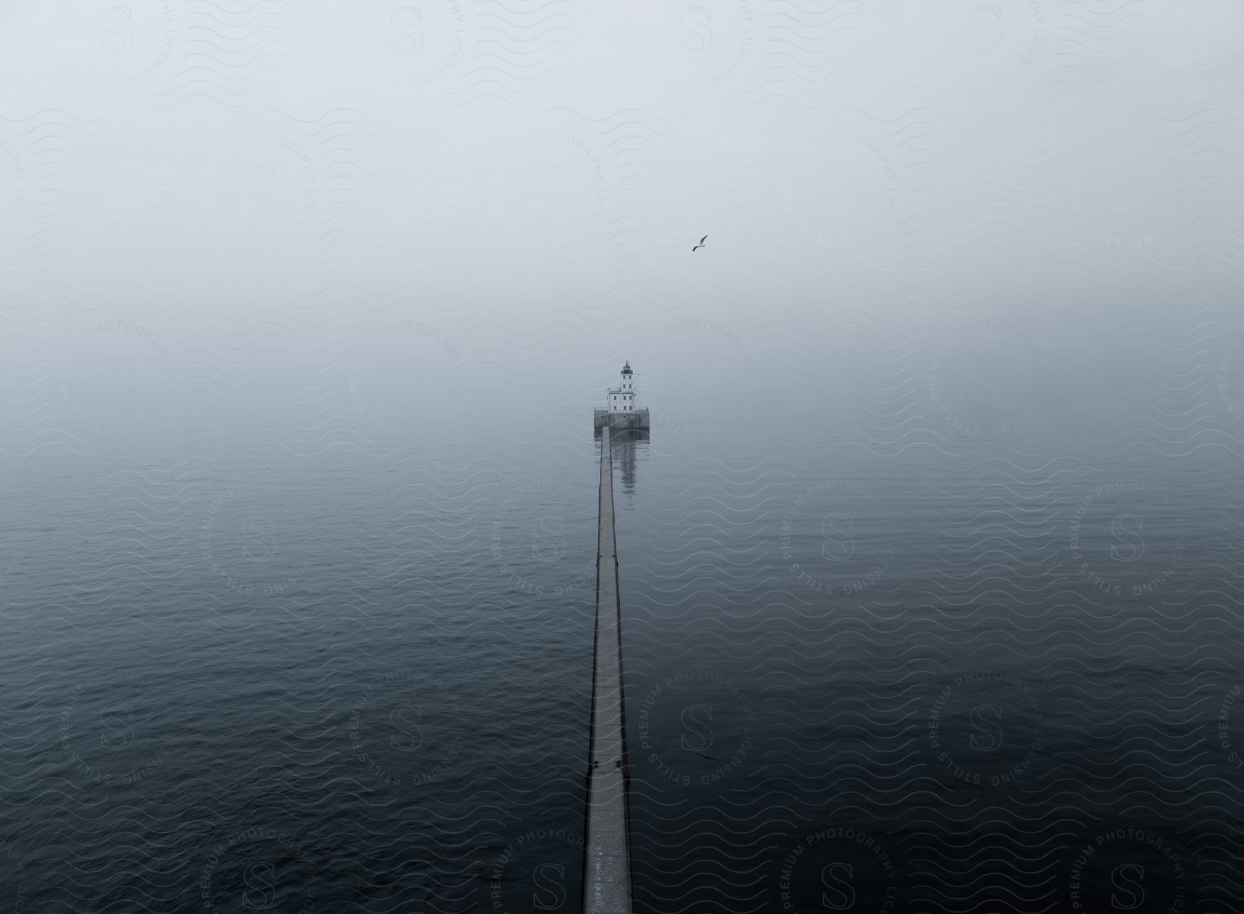 Stock photo of a bridge spans across the water leading to a lighthouse with a seagull flying in a foggy sky