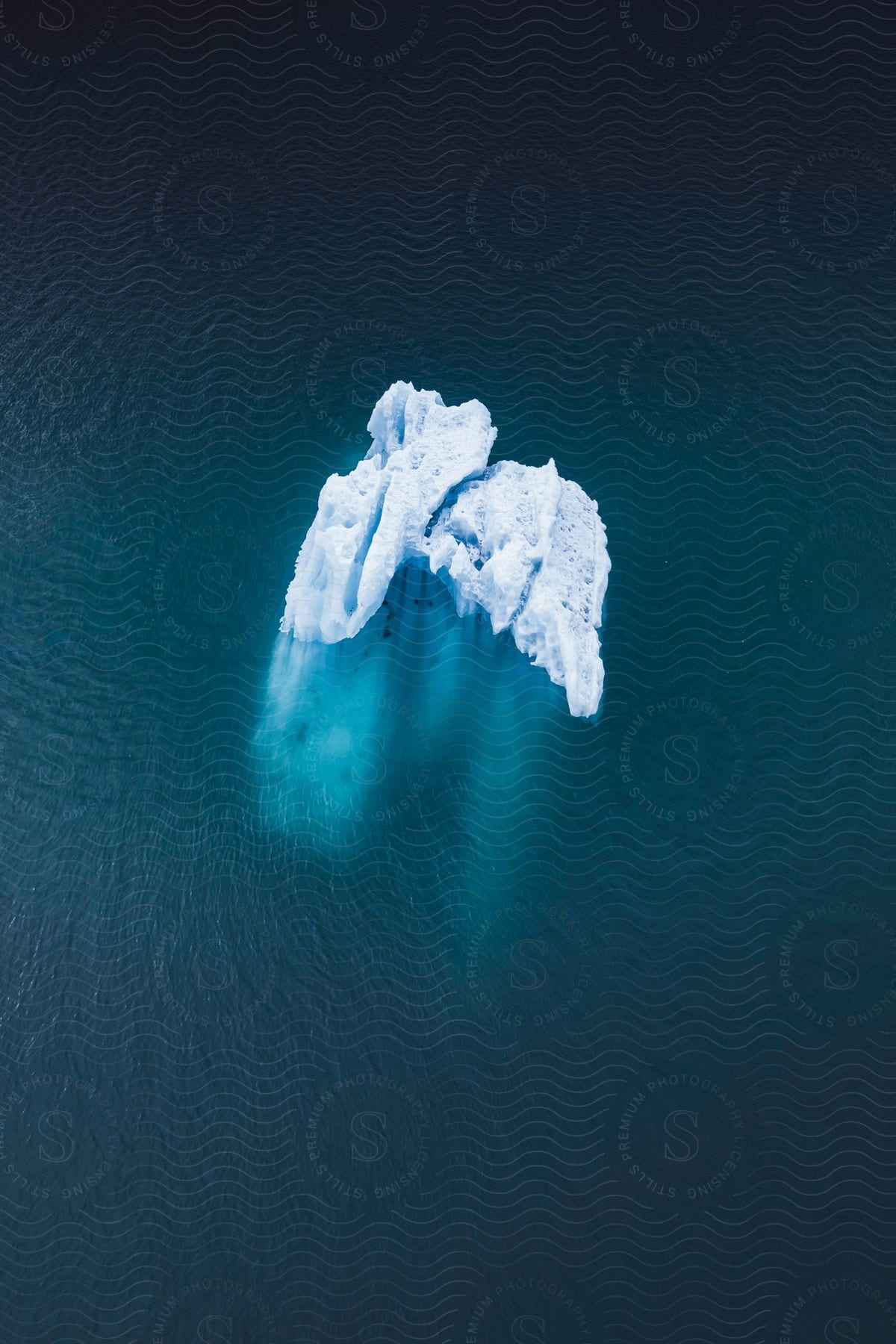 Aerial view of iceberg floating in Arctic Ocean, reflected in calm water.