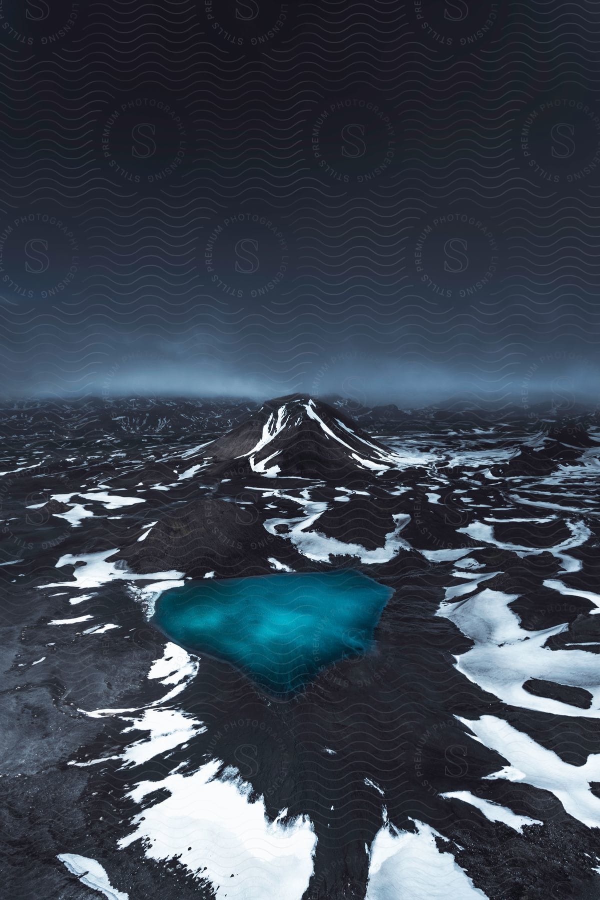 Melting Snow On Mountain Slopes Leading To A Blue Mountain Lake Under A Dark Sky