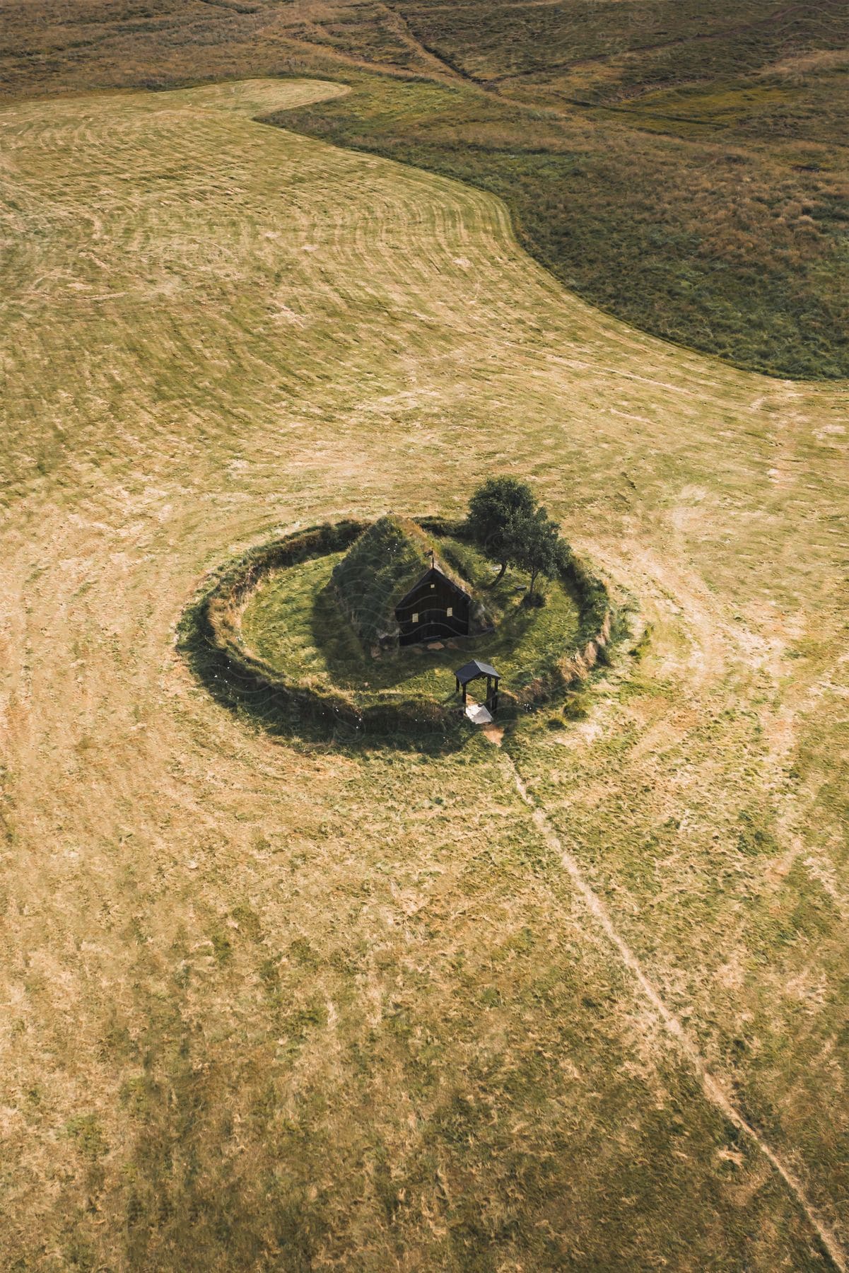 Stock photo of a house with the roof covered in grass and a circular garden in the middle of a field.