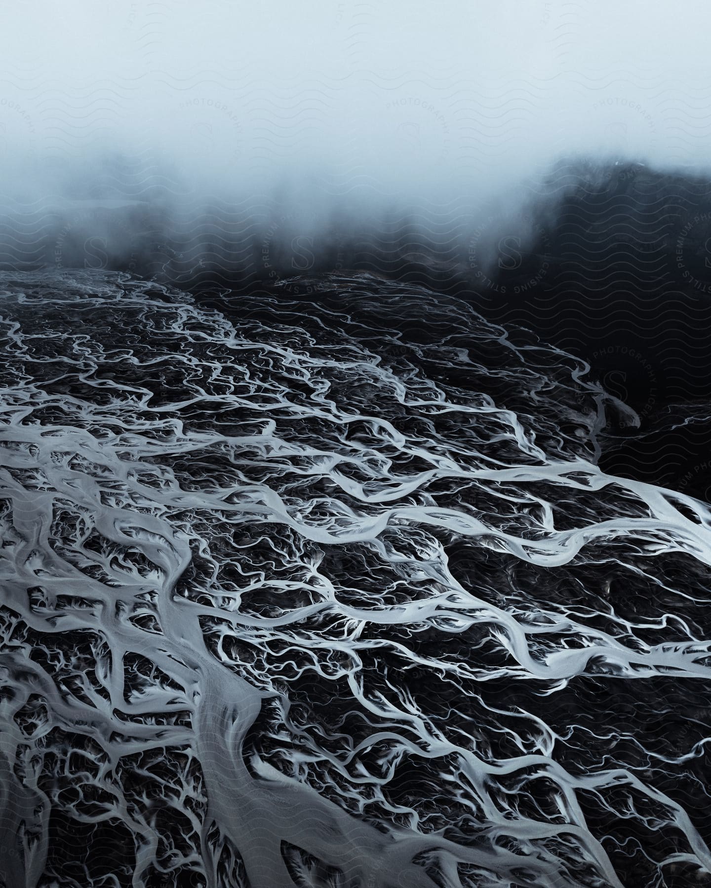 Stock photo of frozen rivulets cover black terrain on foggy day.