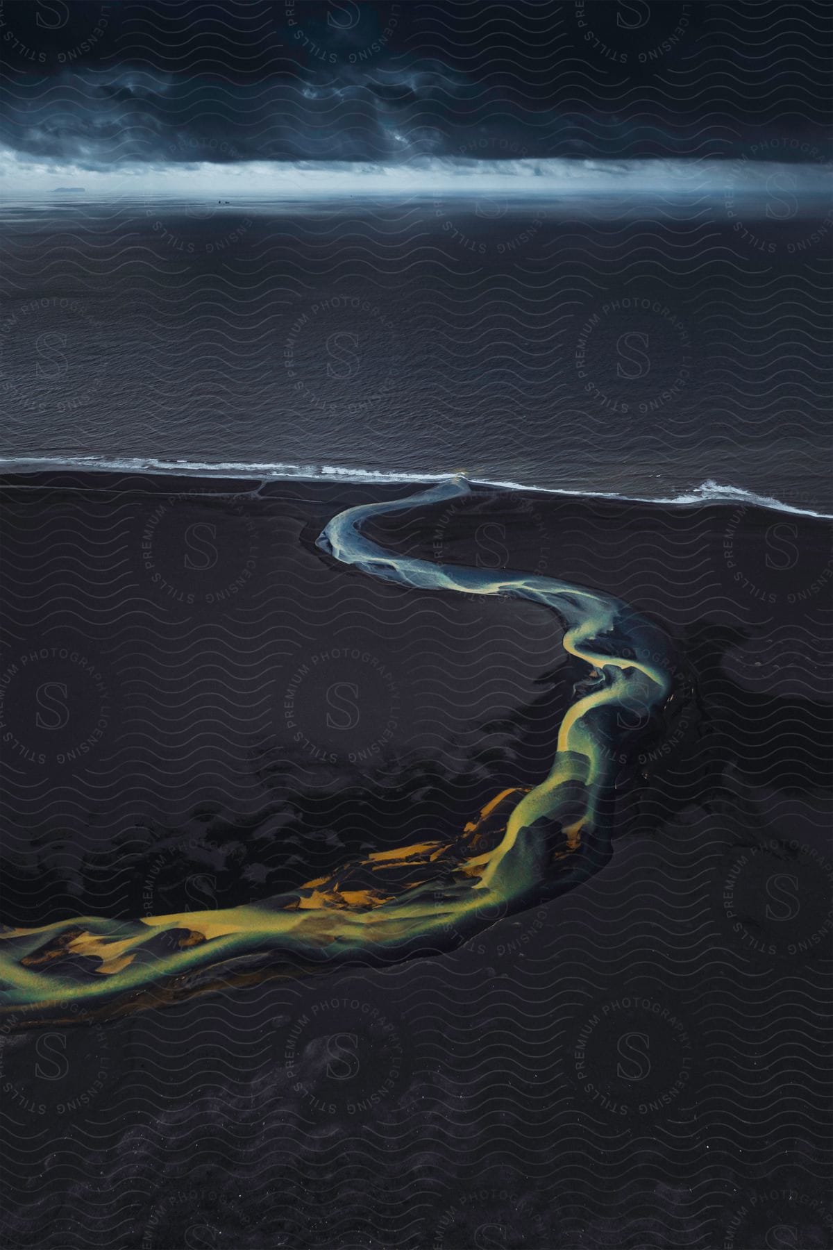 A sulphureous stream flows through a black sand beach towards the ocean