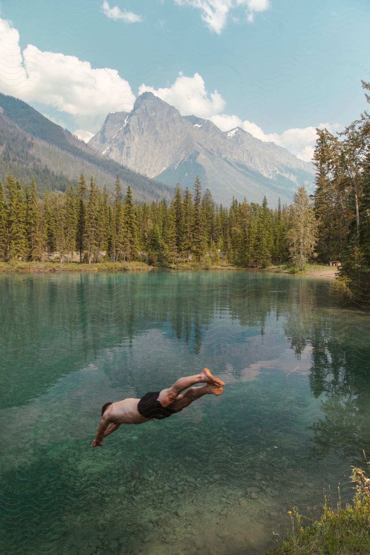 A man swimming in a river surrounded by trees with a mountain view and clear clouds