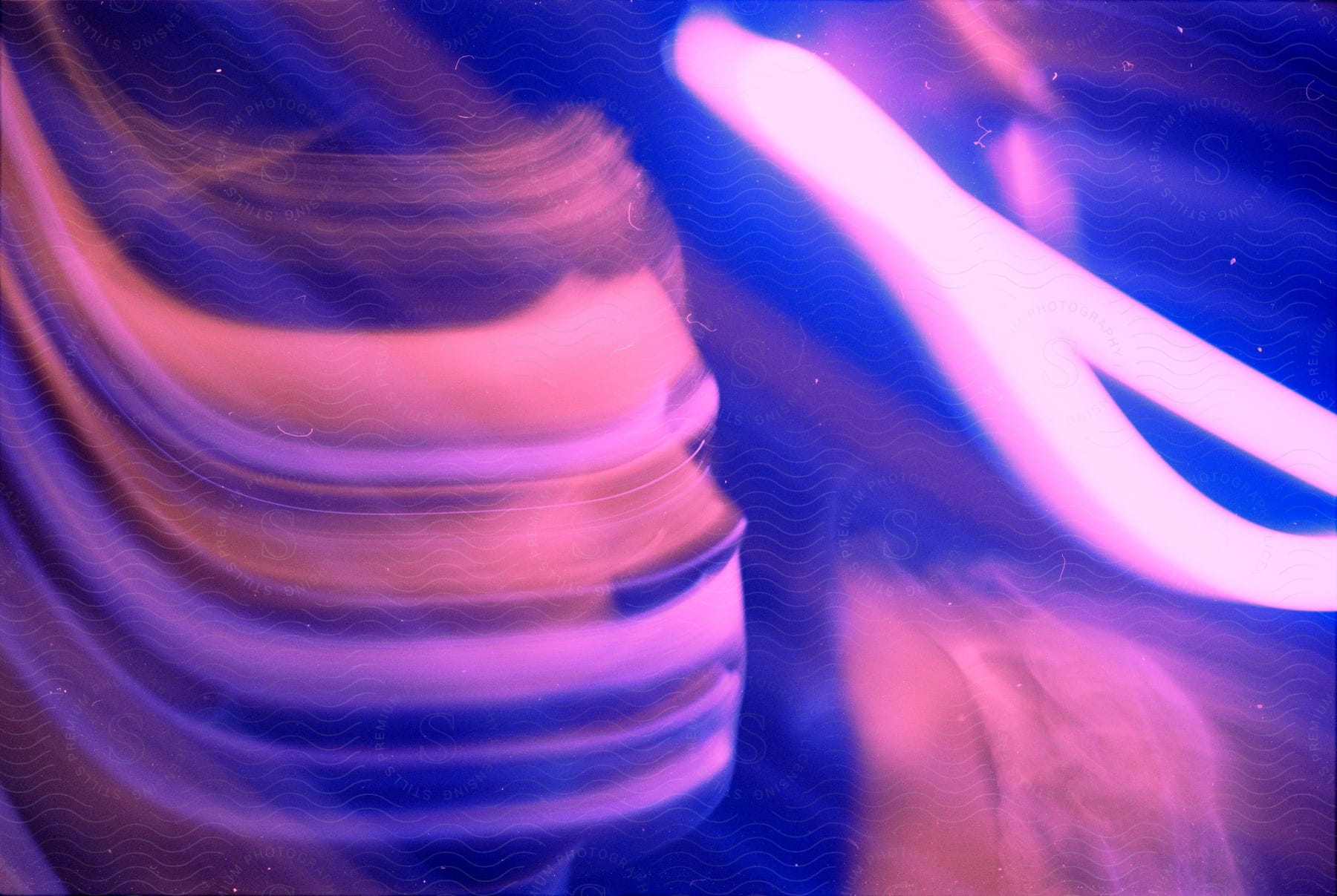 Blurred face surrounded by blue and pink light streaks in a nighttime interior setting