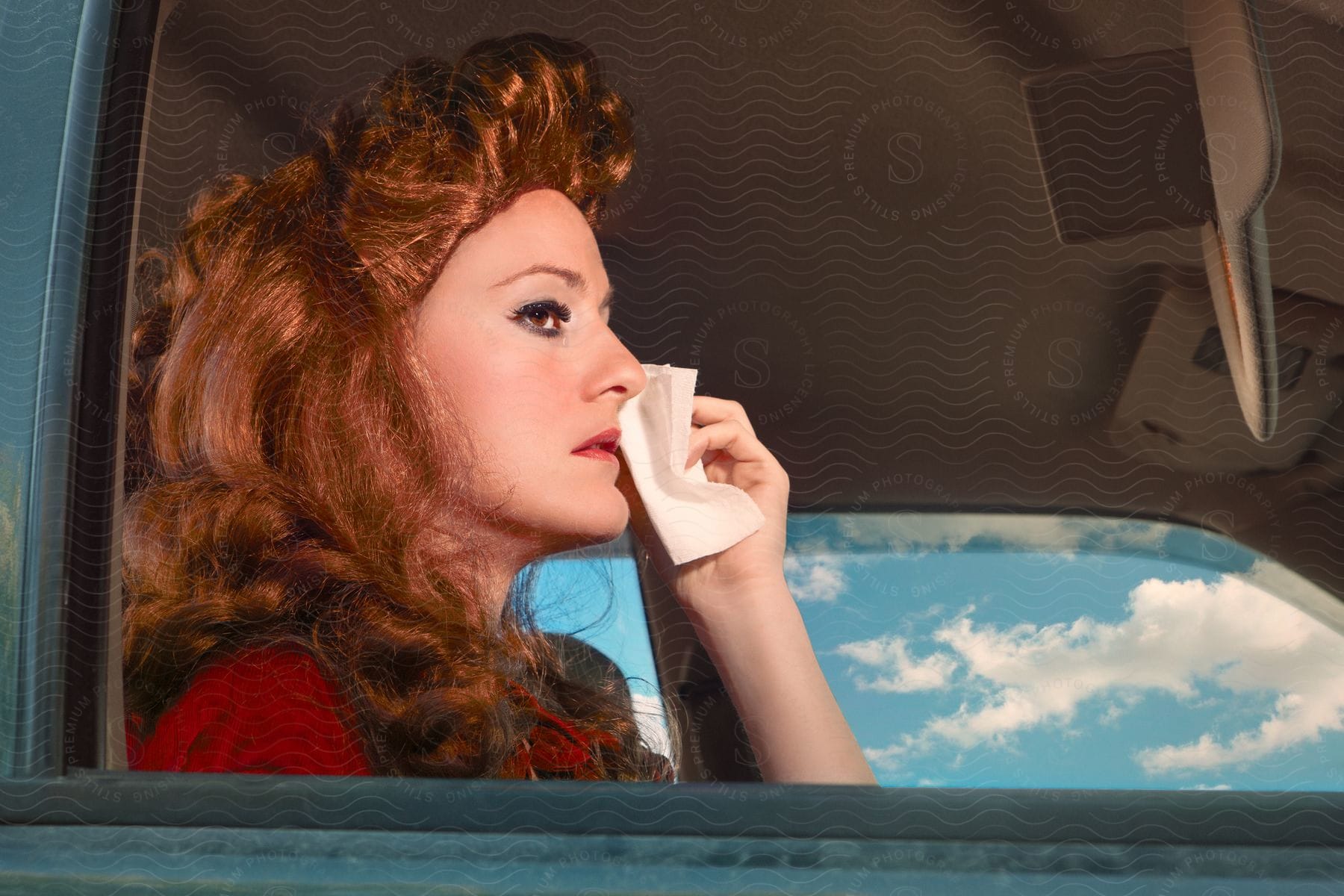 A woman with long red hair is sitting in a truck as she holds a napkin near her face
